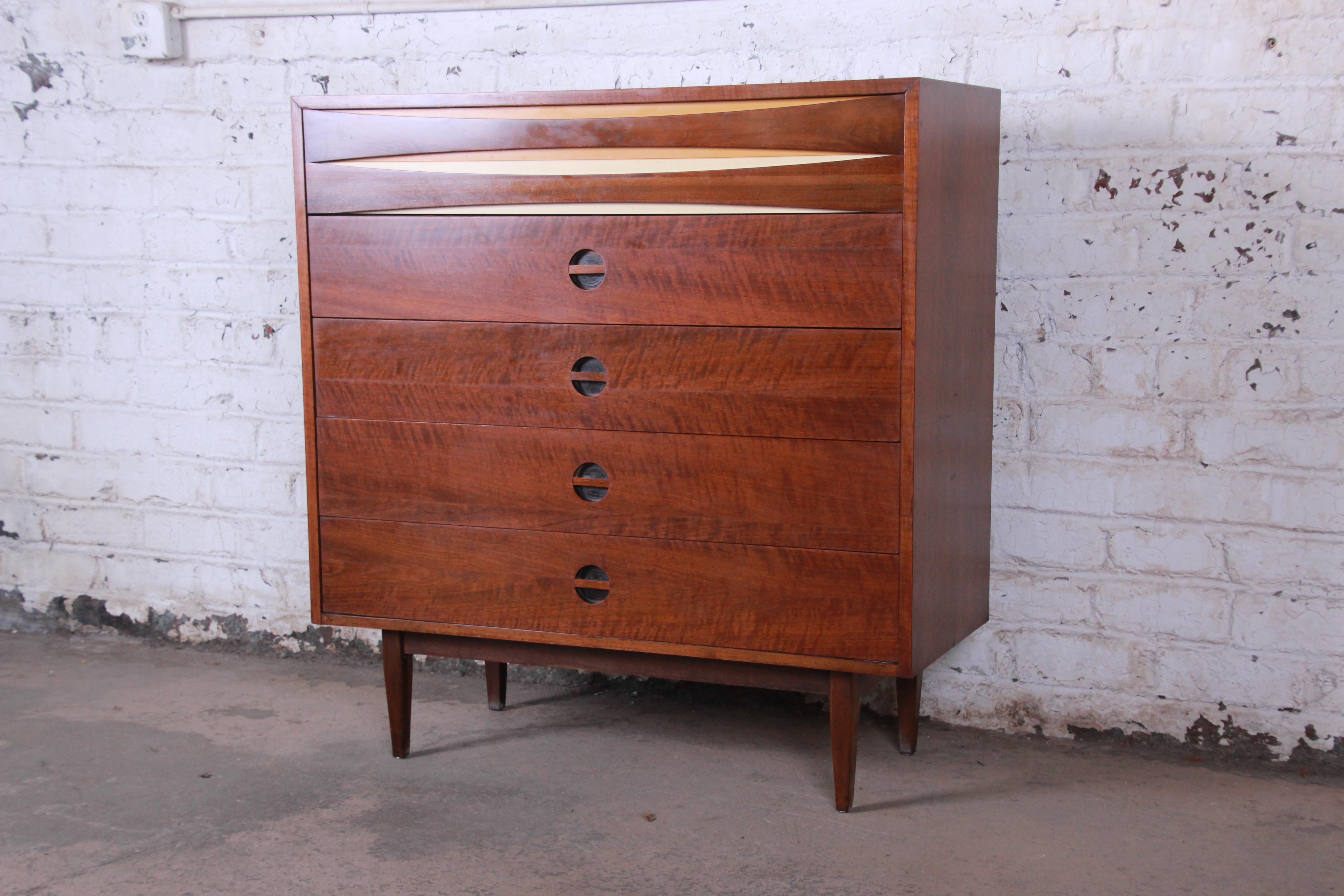 A gorgeous Mid-Century Modern walnut highboy dresser in the style of Arne Vodder. The dresser features beautiful walnut wood grain and a unique bowtie design on the top drawer front. It offers ample room for storage, with five deep dovetailed