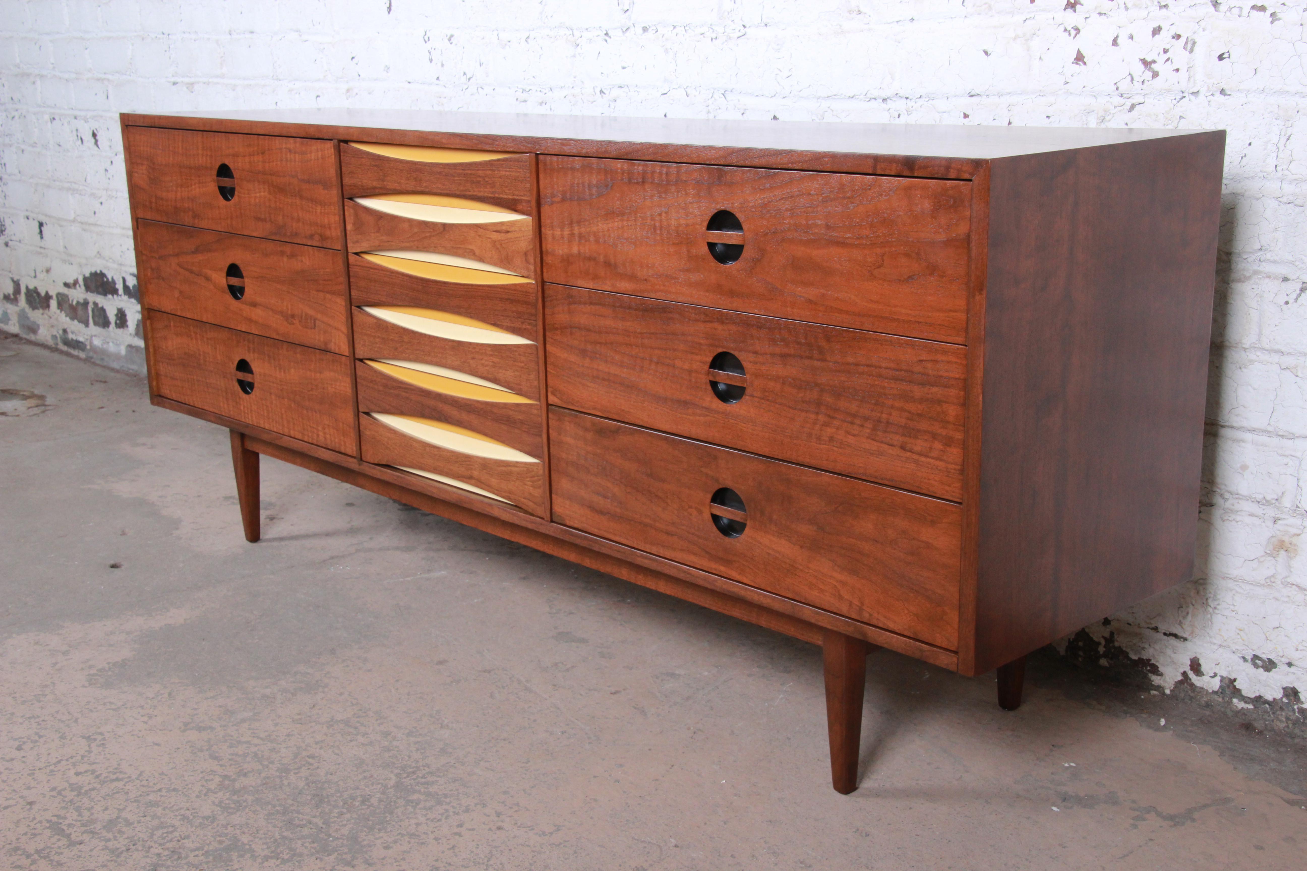 An exceptional Mid-Century Modern Arne Vodder style walnut triple dresser or credenza by West Michigan Furniture Co. The dresser features beautiful walnut wood grain with sculpted recessed drawer pulls. It offers ample storage, with nine deep