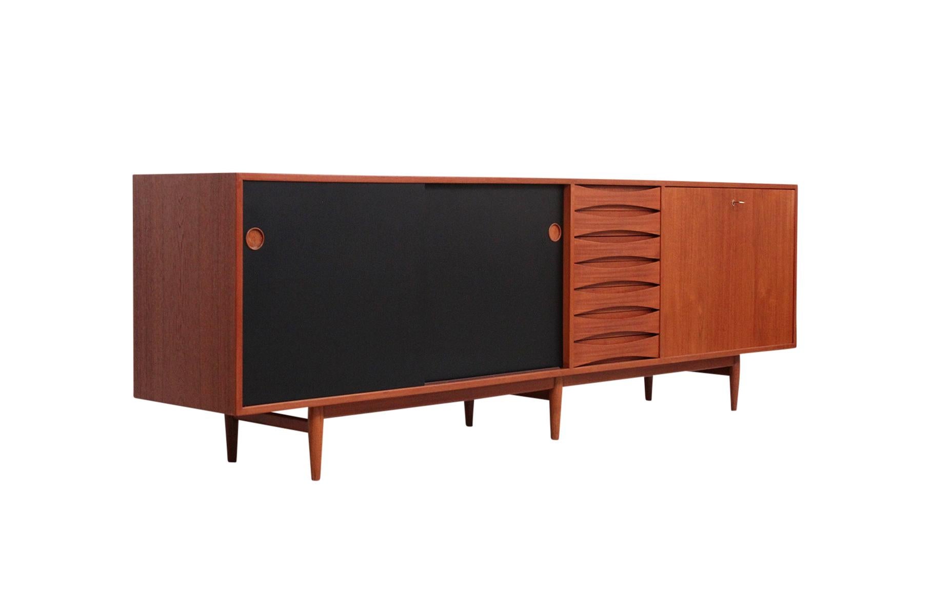 Iconic “Triennale” sideboard credenza designed by Arne Vodder for Sibast. This configuration with teak case, black enamel and teak reversible doors, drop down cabinet, and center pedestal of classic Vodder designed drawers.