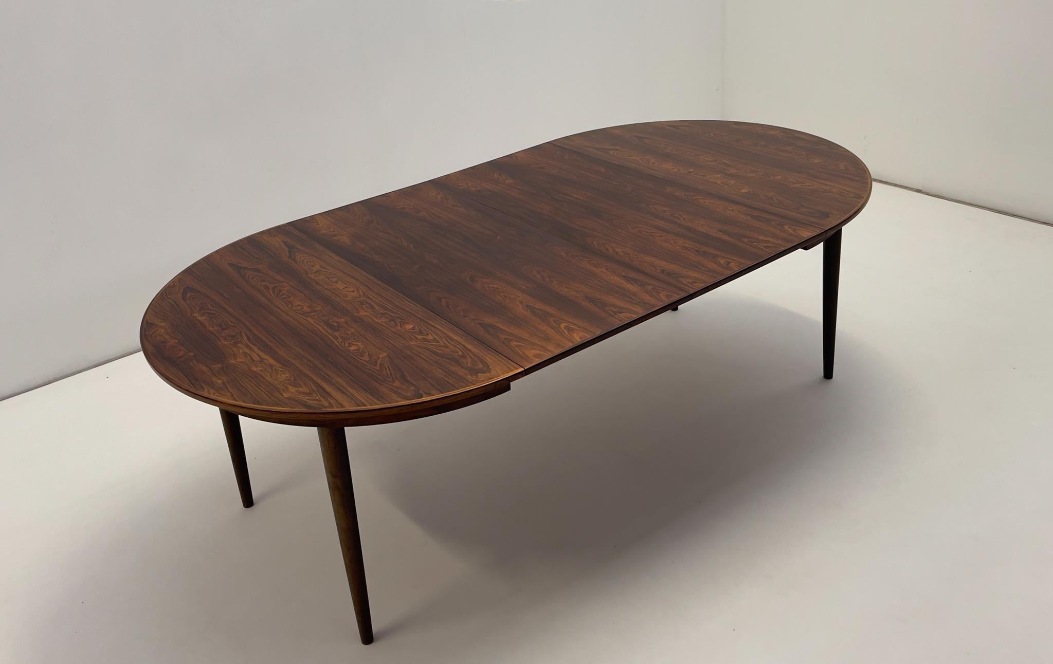 This elegant dining table by Arne Vodder for Sibast is crafted in luxurious hardwood, showcasing its stunning natural grain. Designed in the 1950s, it features an extendable design, transforming from a round to an oval shape to accommodate more