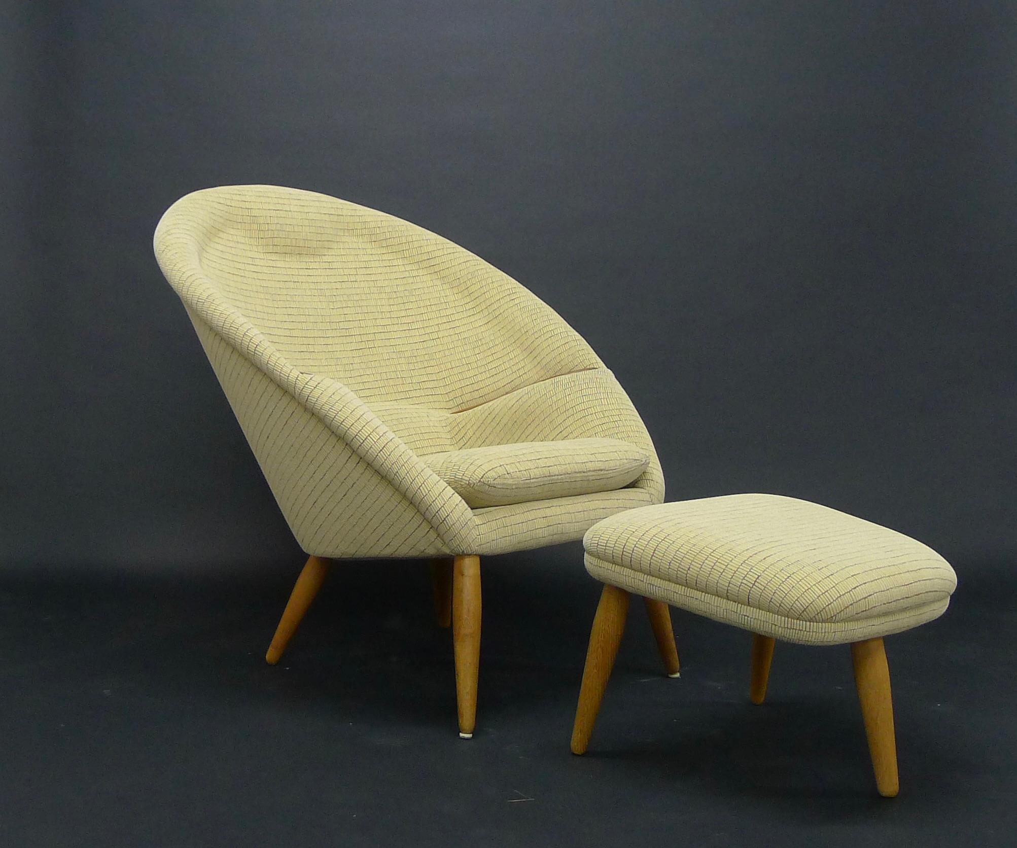 Oda chair and matching ottoman, designed in 1957 by Arnold Madsen, with oak legs and armrests, sympathetically reupholstered in soft ochre textured fabric.

This iconic chair has a horseshoe shaped construction with integrated headrest and inset