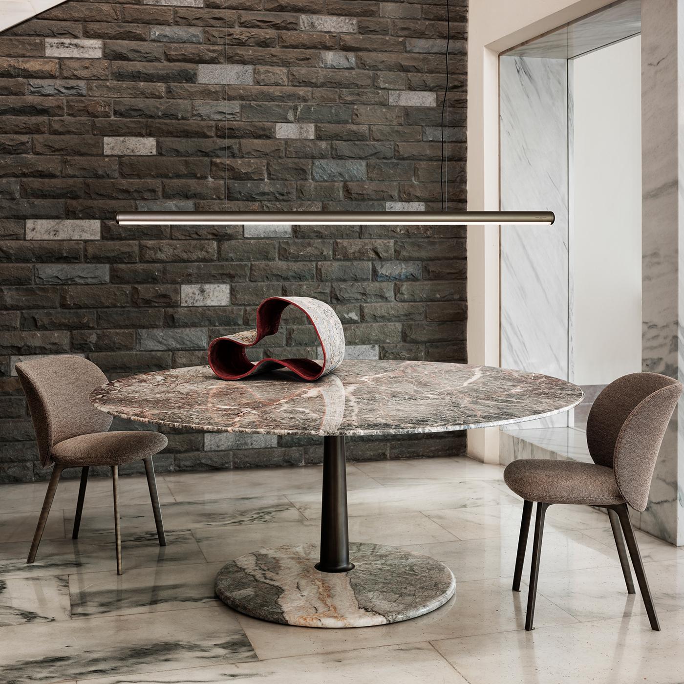 The Arnold dining table features a refined geometric design combining a tapered column, a slim rounded edge tabletop, and a stable truncated cone base. The elegant brass column joins the top and base seamlessly, creating a balanced composition of