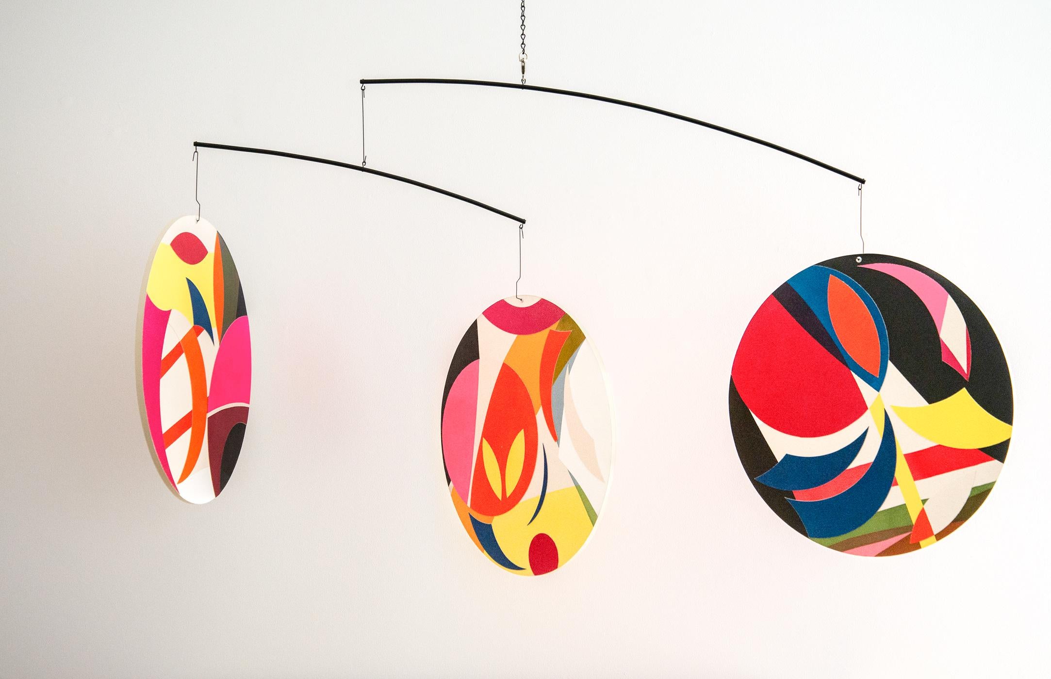 Dynamic and whimsical, Aron Hill’s mobile is a joyful contemporary kinetic sculpture. Three separate discs are covered in a curated collage of shapes and brilliant colours. The colour profile here is Hill’s characteristically vivid palette-- orange,