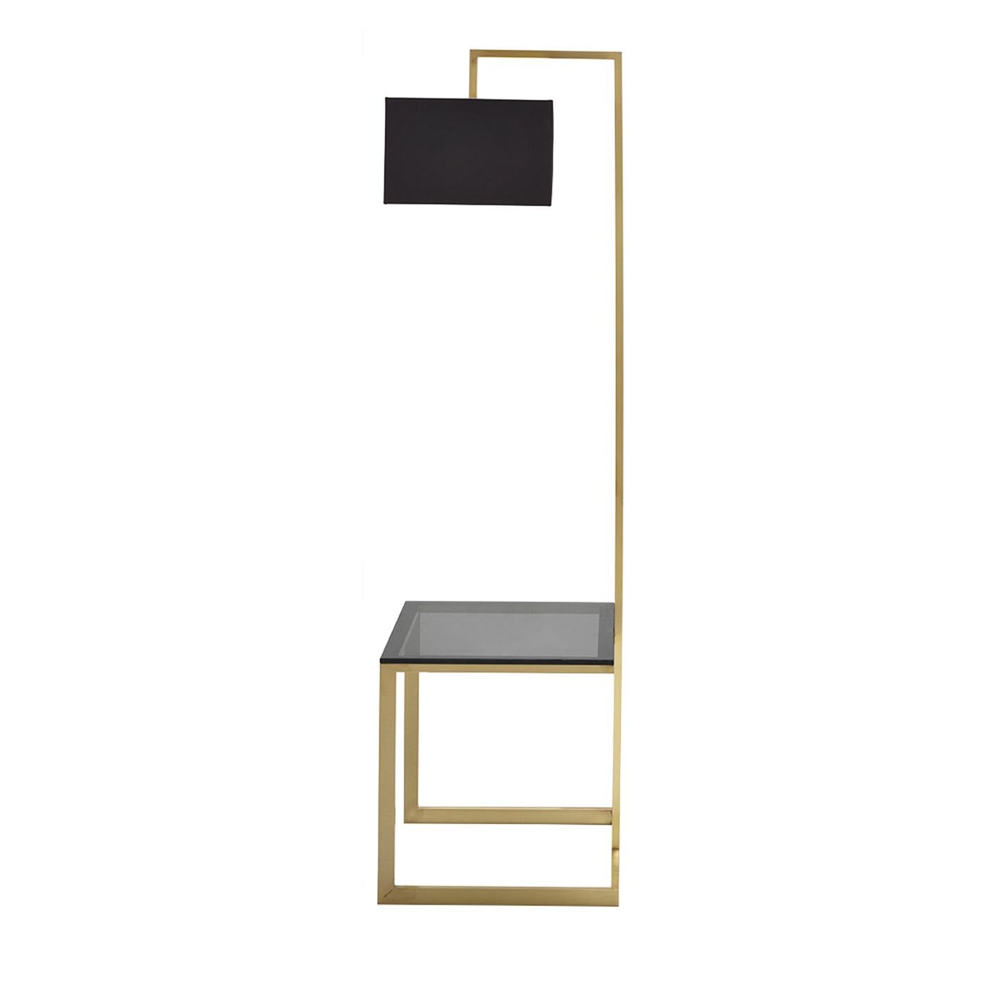 Die Stehleuchte Arona ist Lichtquelle und Beistelltisch in einem und wurde für minimalistische Wohnräume entworfen. Der Tisch steht auf einem Sockel aus brüniertem Messing und hat eine Platte aus rauchfarbenem Glas, die für einen eleganten Effekt
