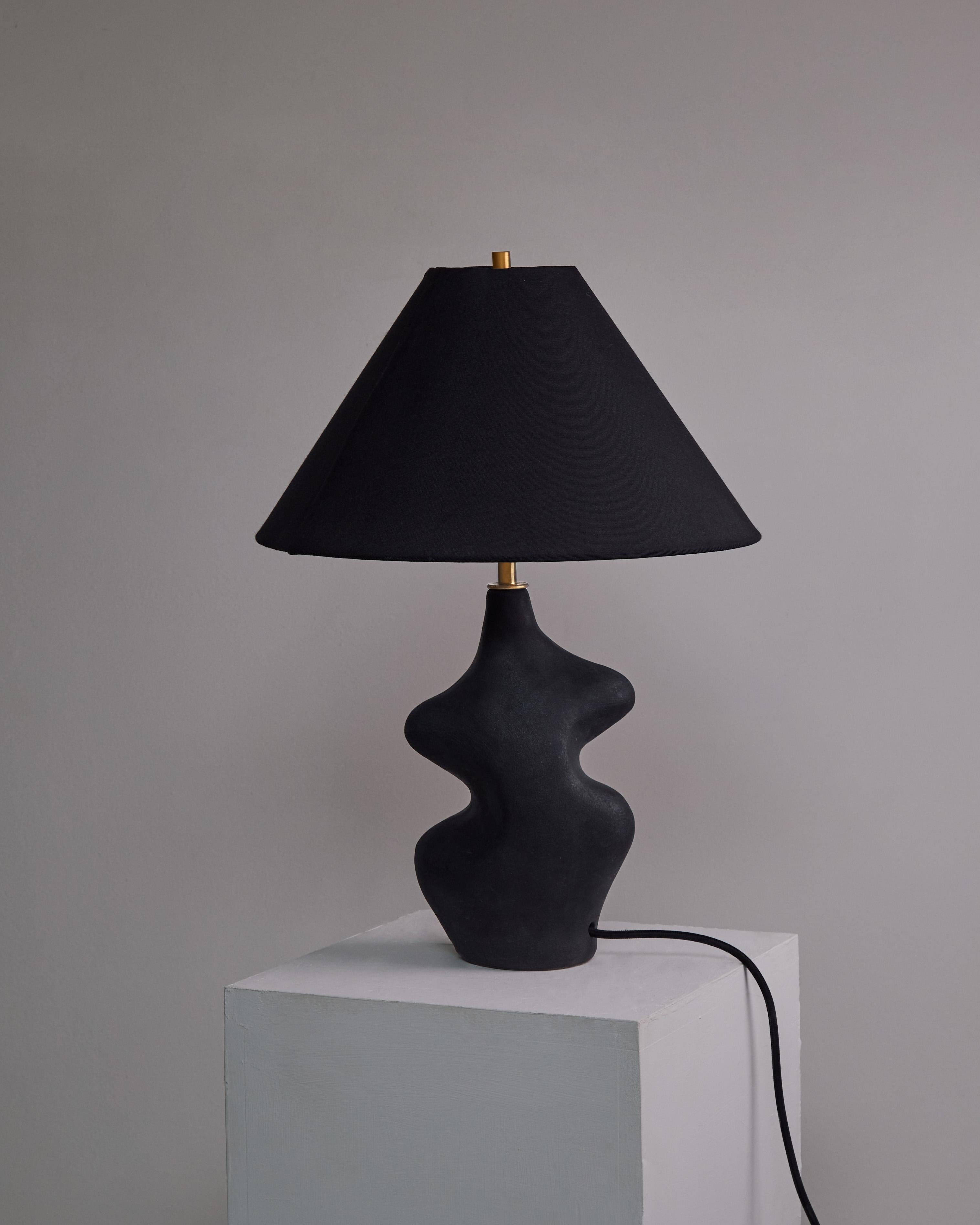 Lampe de table sculpturale Arp Black par Hanna Englund Ceramics
Hauteur de 49 cm, abat-jour compris, diamètre de l'abat-jour 35 cm.
MATERIAL : Grès, céramique, laiton brut, lin.
Lampe de table en céramique, sculpturale et incurvée, faite à la main.
