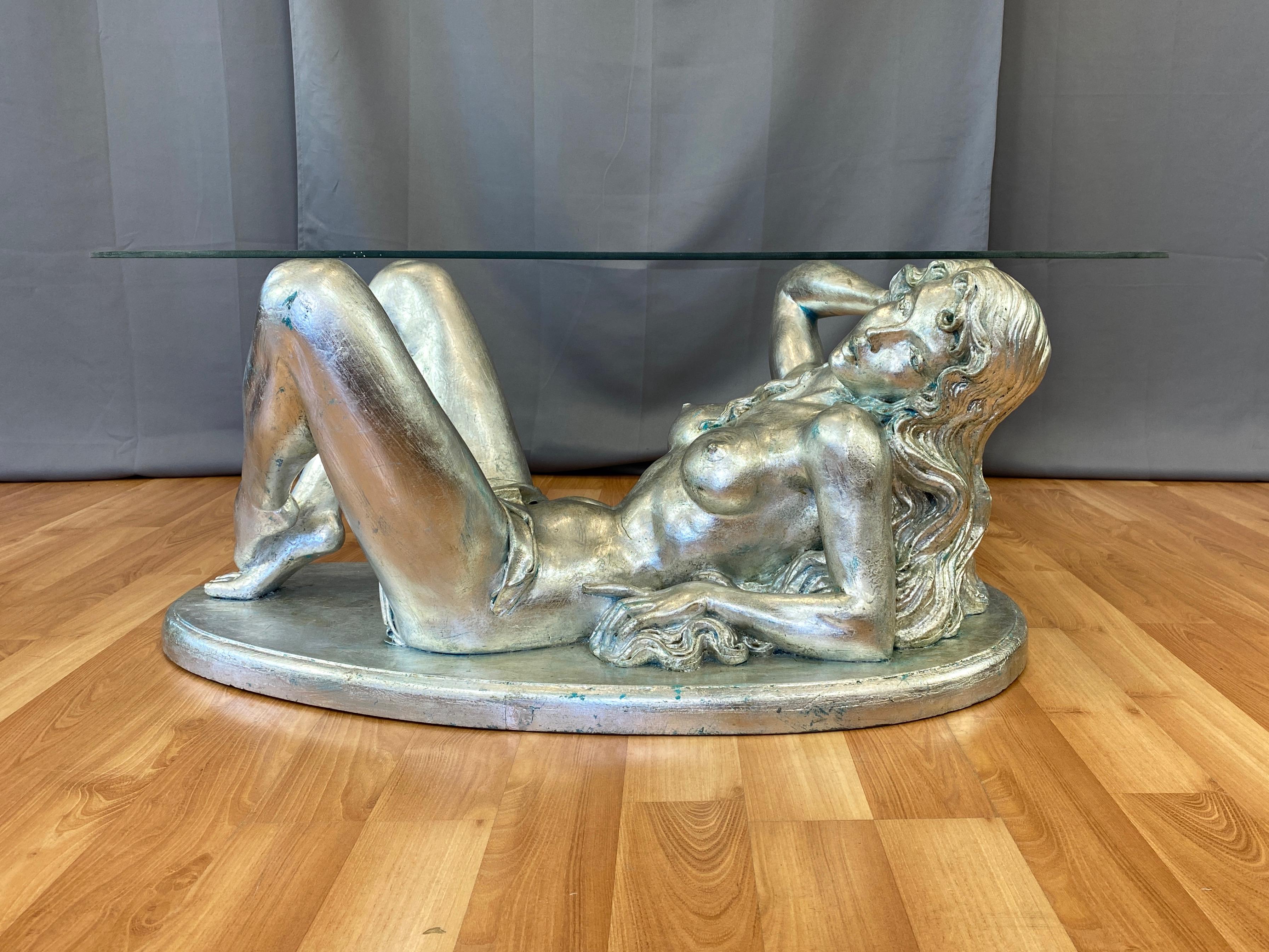 An alluring 1960s silver-leafed nude female figural coffee table with free-form glass top by ARP.

Beautifully sculpted nearly life-size subject assumes a classical—yet casually provocative—pose. She's adorned in nothing more than a tastefully