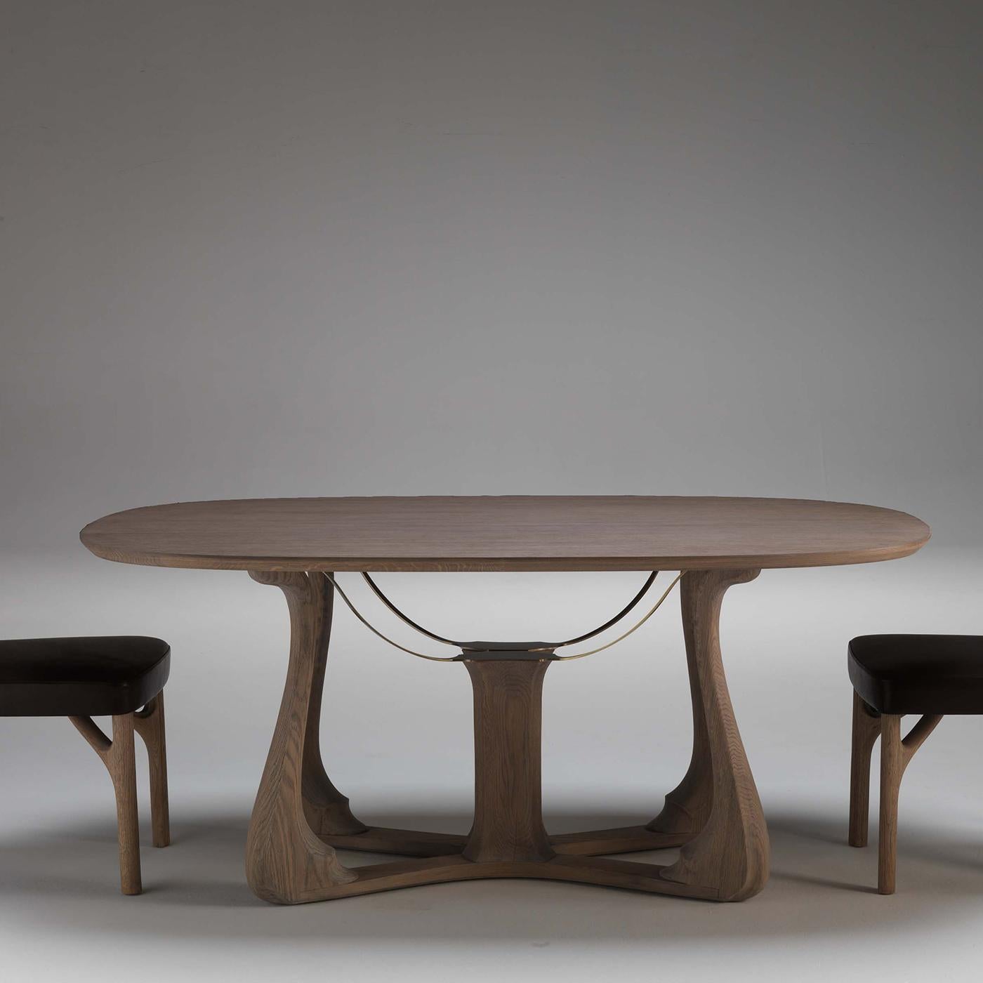 The stunning base of this dining table evokes the body of a harp, hence its name in Italian. Entirely made of oak wood, its four sinuous legs cross at the center, giving a serene and elegant look to the piece. From the central element four metal