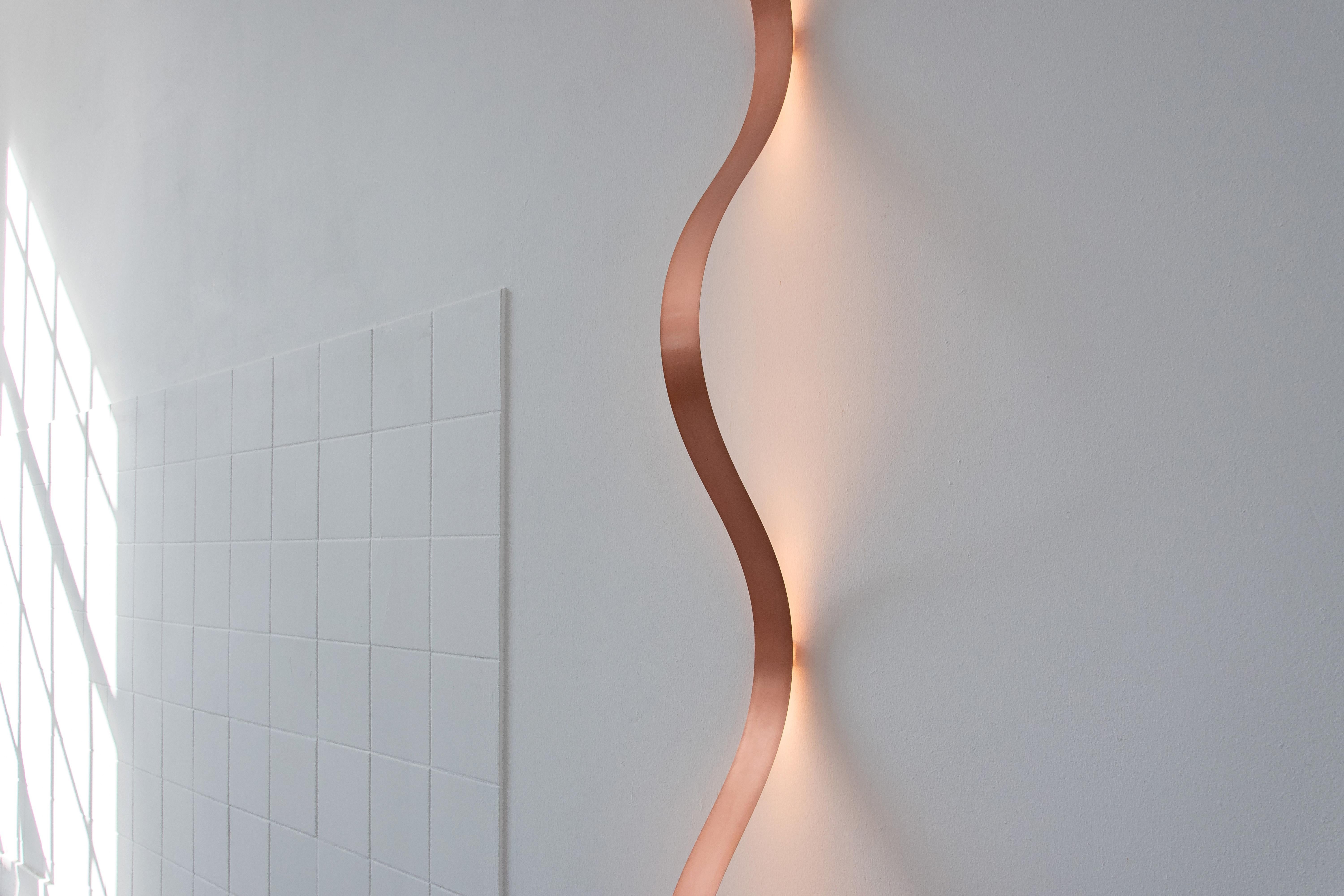 The Sine Lights are made out of powdercoated spring steel strips. By fixing the lamp to the wall or ceiling with small brackets, the wave form appears as a result of the tension in the material.

The LED lighting on the back gives of a pleasant