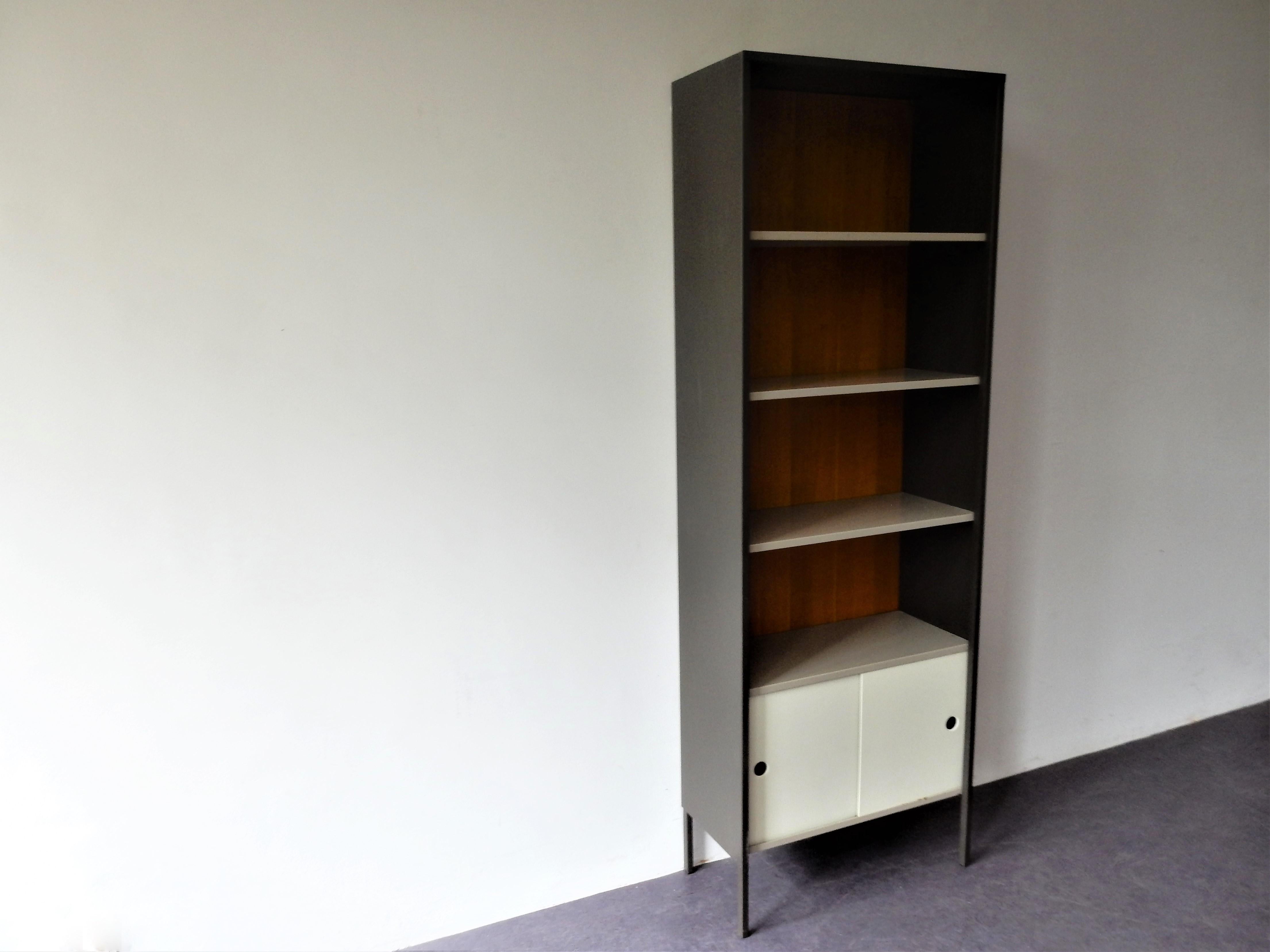 This elegant bookcase was designed by Coen de Vries for Pilastro in the 1960's. It has a dark grey metal frame with a nice wooden backpanel. It comes with 3 grey metal shelves and at the bottom a metal cabinet with 2 white sliding doors. We have