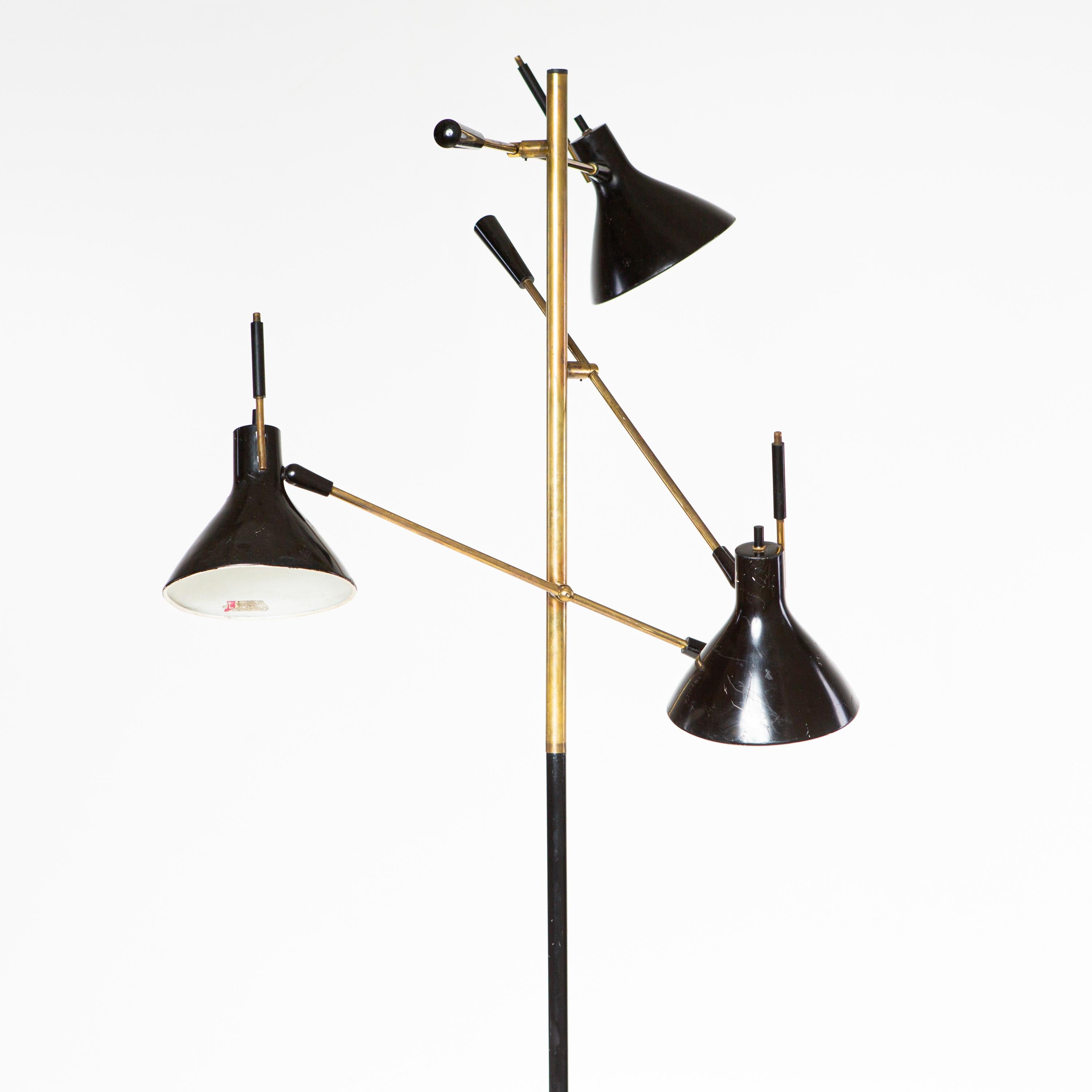 Large floor lamp standing on a round marble base with black shaft and three brass arms. These are adjustable in inclination and end in conical black lampshades. Labeled 