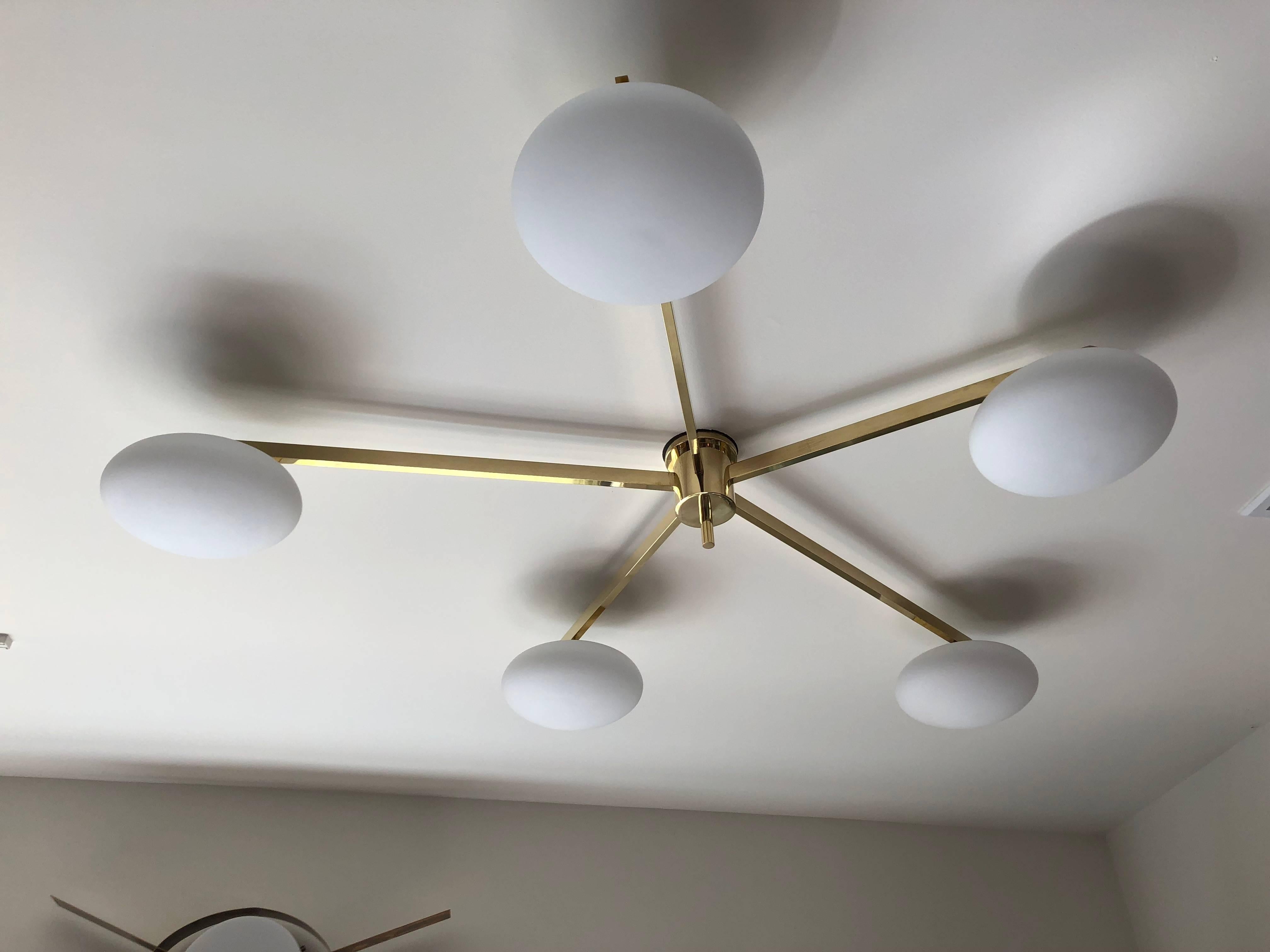 Five brass arms of different lengths emanate from a centre brass column to create this modern asymmetric classic ceiling fixture. Beautiful handblown white glass globes suspend at the end of each arm. All parts are in keeping with production
