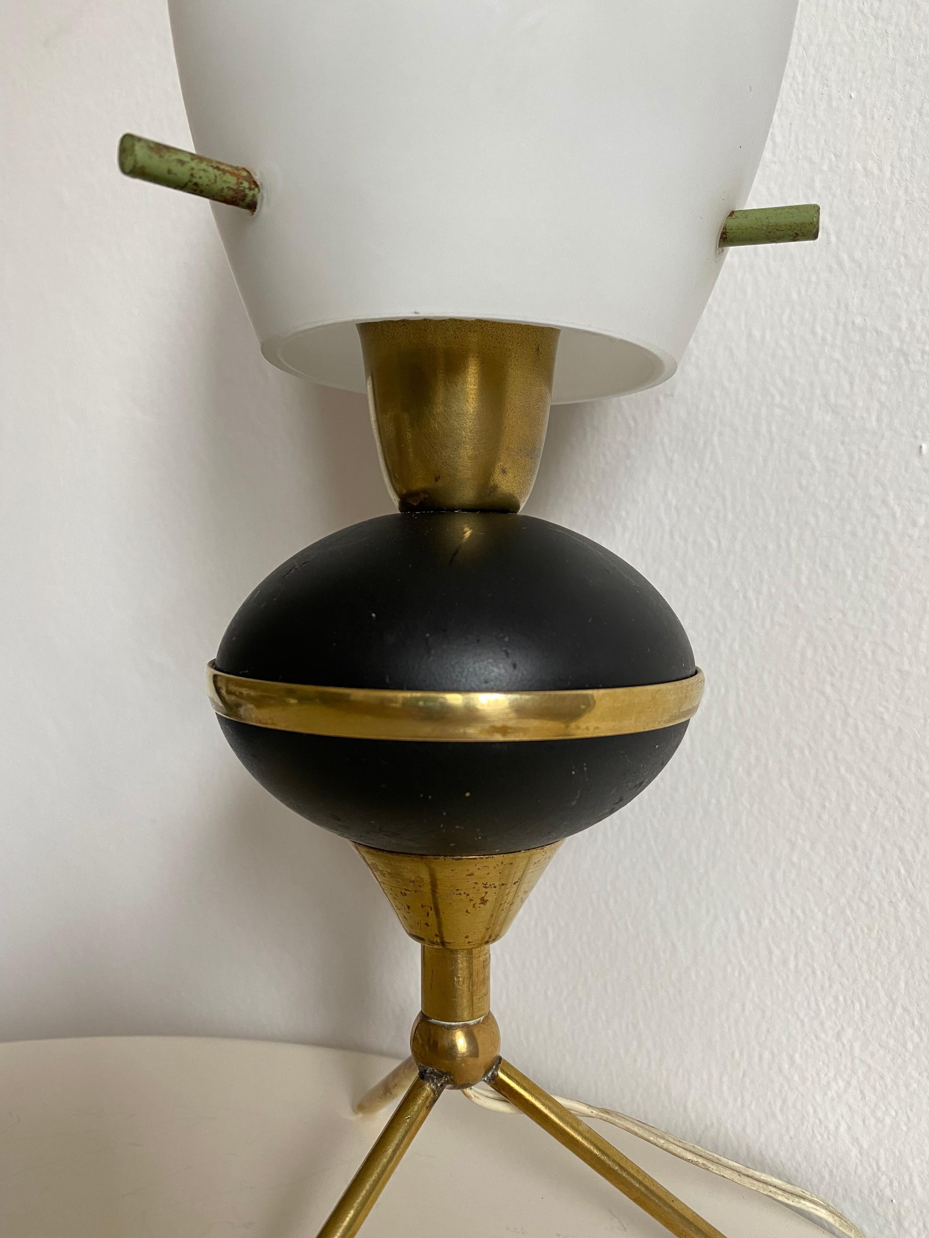 Italian manufactured small table lamp in the style of Angelo Lelii (Lelli) for Arredoluce.

Brass center band dissects the small black painted brass orb which is held up by three skinny brass feet. Oval opaline glass orb.

Adorably sized it