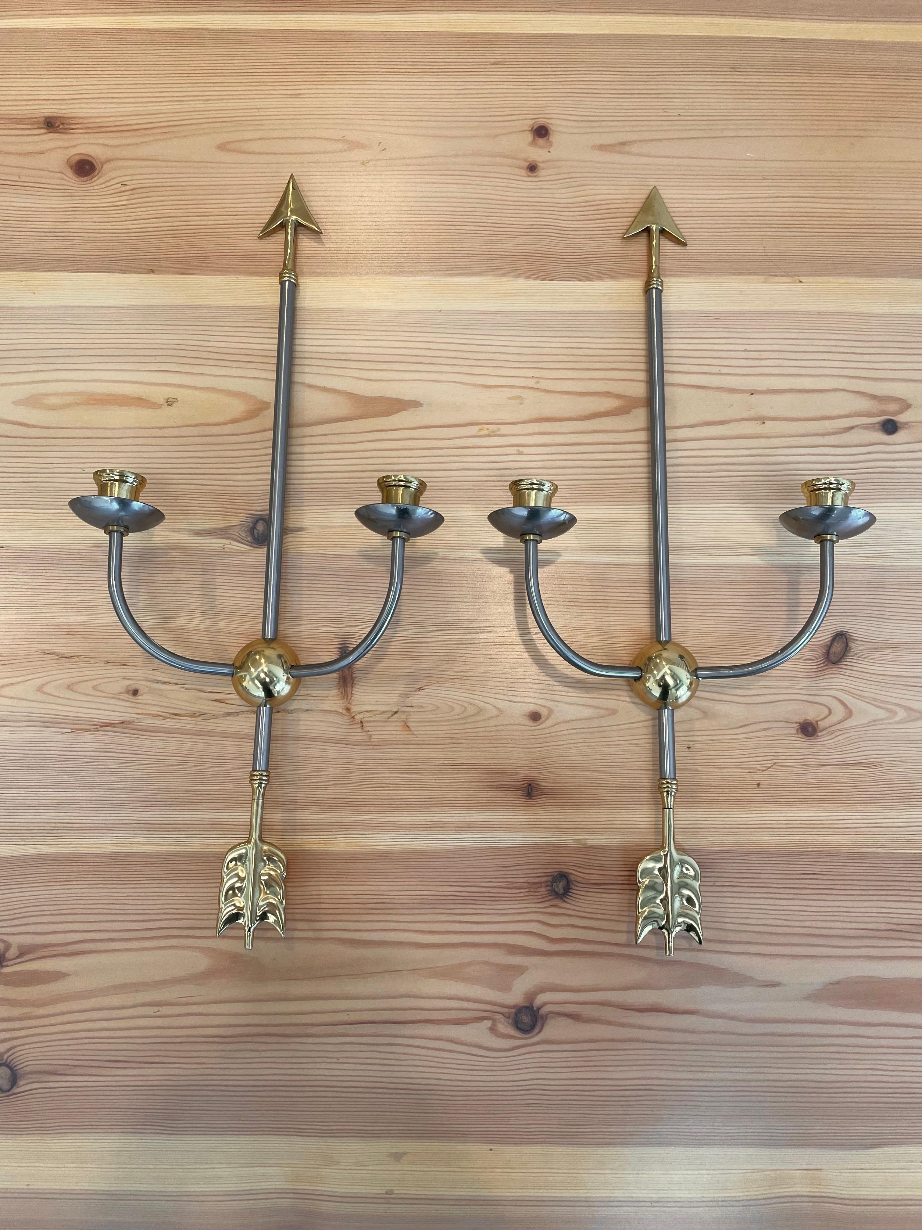 Height: 53cm
Depth: 10cm
Width: 24cm

Date: 1960s. 
Materials: Brass, Metal.

Description: Arrow wall sconces are stylish and versatile lighting fixtures that add a touch of charm and sophistication to any space. Inspired by the classic arrow shape,