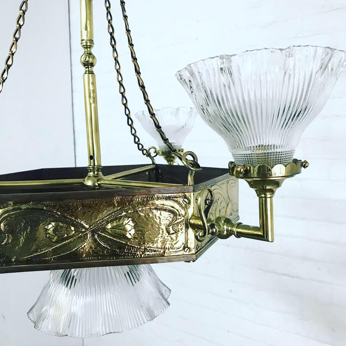 A good quality Art & Crafts brass hanging pendant ceiling light of hexagonal form. The two tiers have repousse floral decoration, with three clear moulded glass shades and one larger central shade. 

Measures: 70cm diameter x 81cm high.