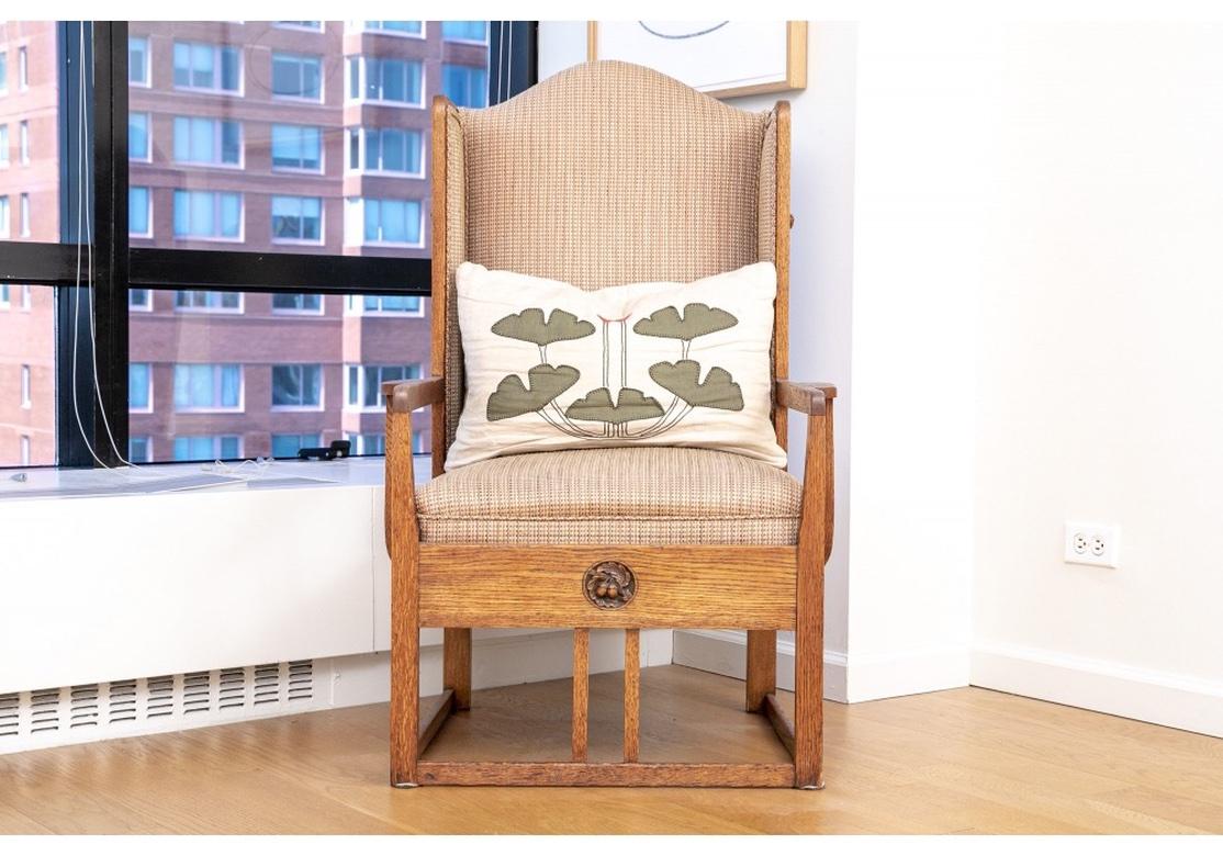 A heavy, solid and sturdy Arts & Crafts oak lounge chair with tight back and inset seat cushion covered in a woven textured multi-colored tweed fabric with double welting. The chair with carved acorn medallions on both sides and apron, the armrests