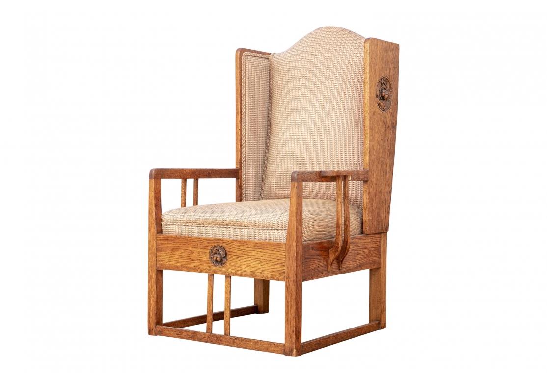 A heavy, solid and sturdy Arts & Crafts oak lounge chair with tight back and inset seat cushion covered in a woven textured multi-colored tweed fabric with double welting. The chair with carved acorn medallions on both sides and apron, the armrests