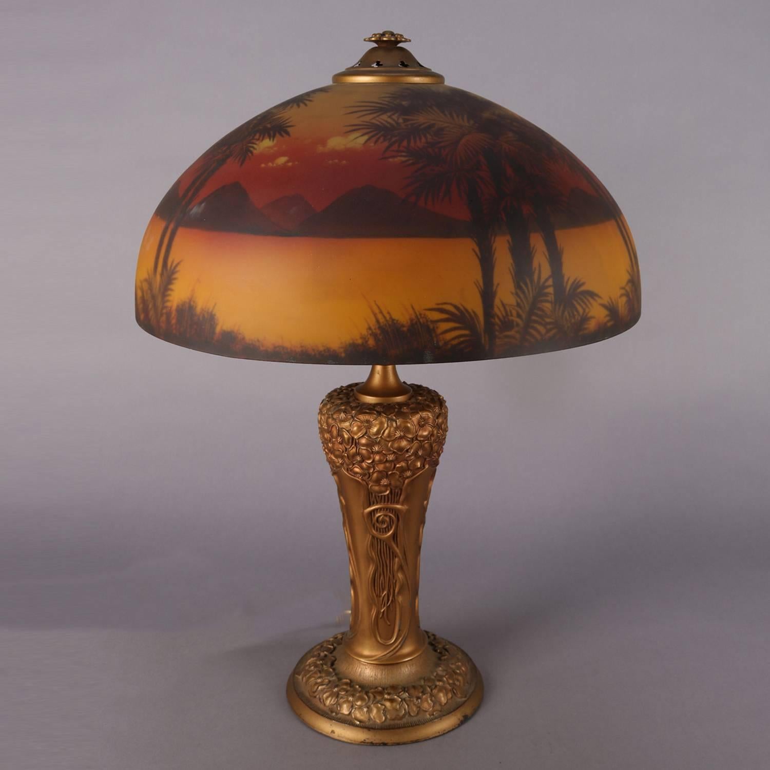 An Arts & Crafts table lamp features gilt and foliate cast base having dual lights with a Phoenix reverse painted dome shade with lake and landscape scene, circa 1910

Measures: 26