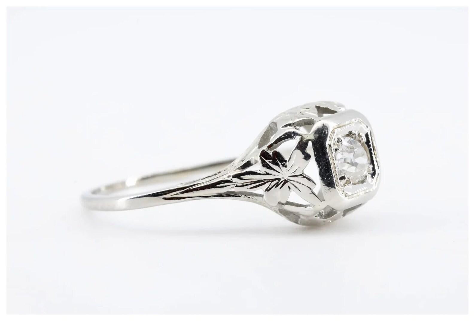 A Art Deco period die struck diamond engagement ring. Crafted in 18 karat white gold and centered by a 0.20 carat Old European cut diamond. Grading as H color VS2 clarity the diamond is embraced by hand engraved detailing and pierced filigree