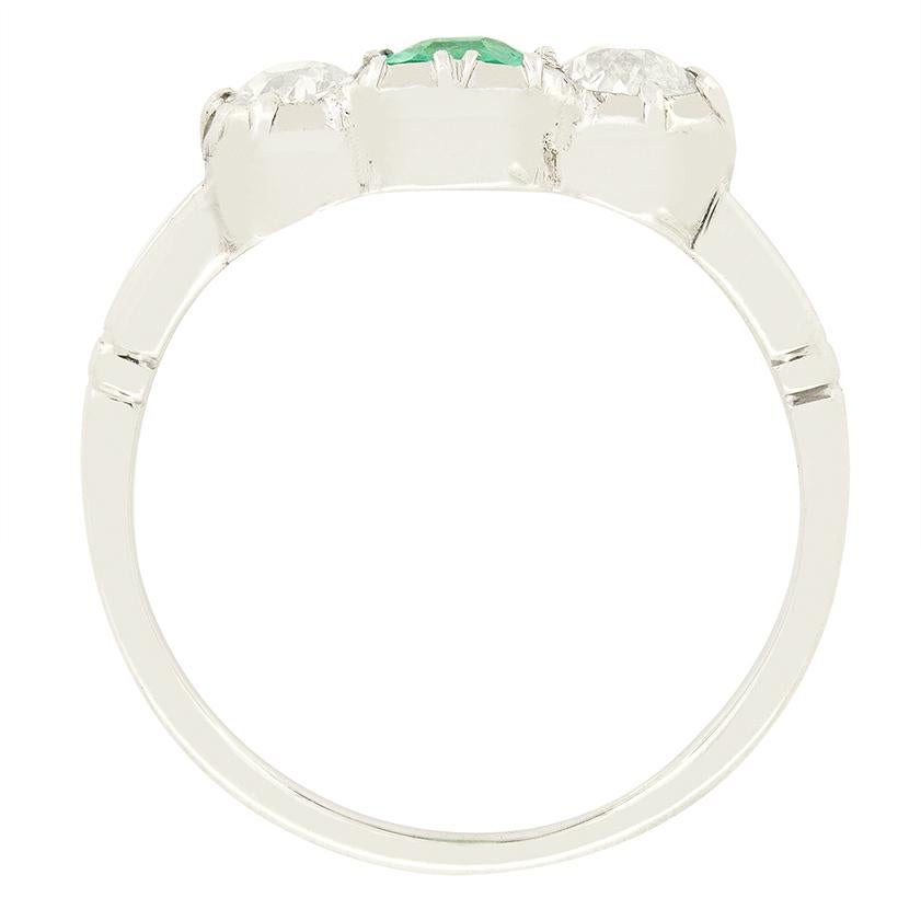 Datant des années 1920, cette magnifique bague trilogie présente une émeraude centrale flanquée de diamants. L'émeraude naturelle est une pierre de taille émeraude classique pesant 0,40 carat. Chacun des diamants qui l'accompagnent pèse 0,25 carat