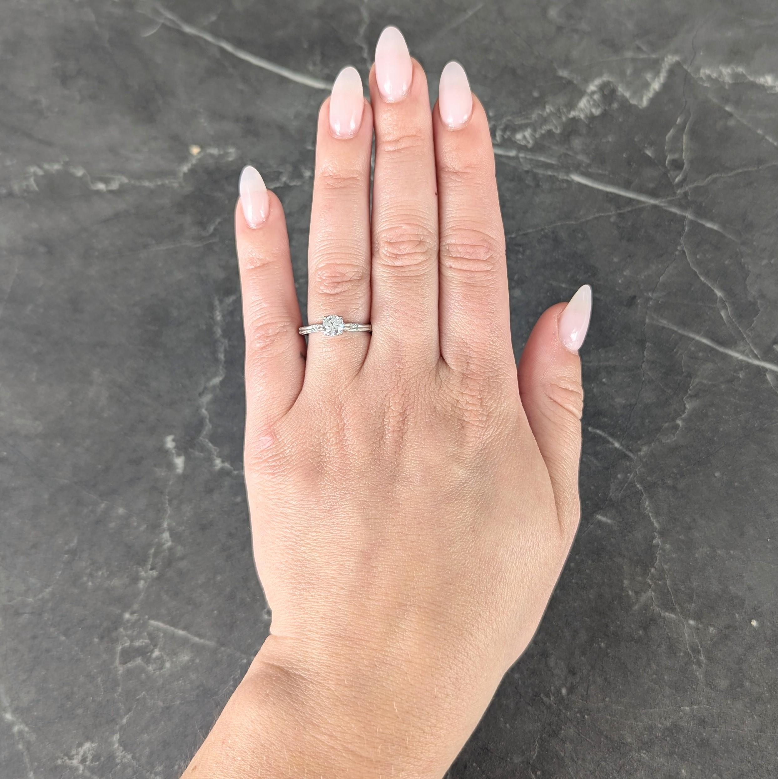 Centering a transitional cut diamond weighing approximately 0.48 carats
H color with VS2 clarity - set via tri-split prongs in pierced basket
Flanked by engraved orange blossom motif cathedral shoulders
Accented by milgrain detail edges
Stamped for