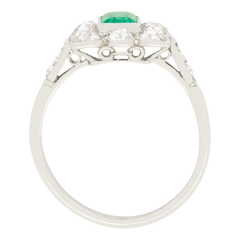 Hailing from France, this beautiful halo ring was made in the 1920s. The central stone is an emerald cut, natural, forest green Emerald, weighing 0.50 carat. The rub over set stone has been surrounding by a beautiful cluster of old cut diamonds.