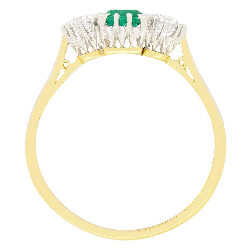Dating back to the 1920s is this gorgeous Emerald and diamond trilogy ring. The vivid green Emerald is an emerald cut stone weighing 0.50 carat. A pair of sparkling transitional cut diamonds are set to either side. Each diamond weighs 0.20 carat and