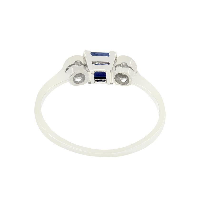 Dating back to the 1920s, this Art Deco trilogy ring features a square cut central sapphire flanked by old cut diamonds. The vivid blue sapphire weighs 0.50 carat and sits within platinum corner claws. Each of the flanking diamonds match in size and
