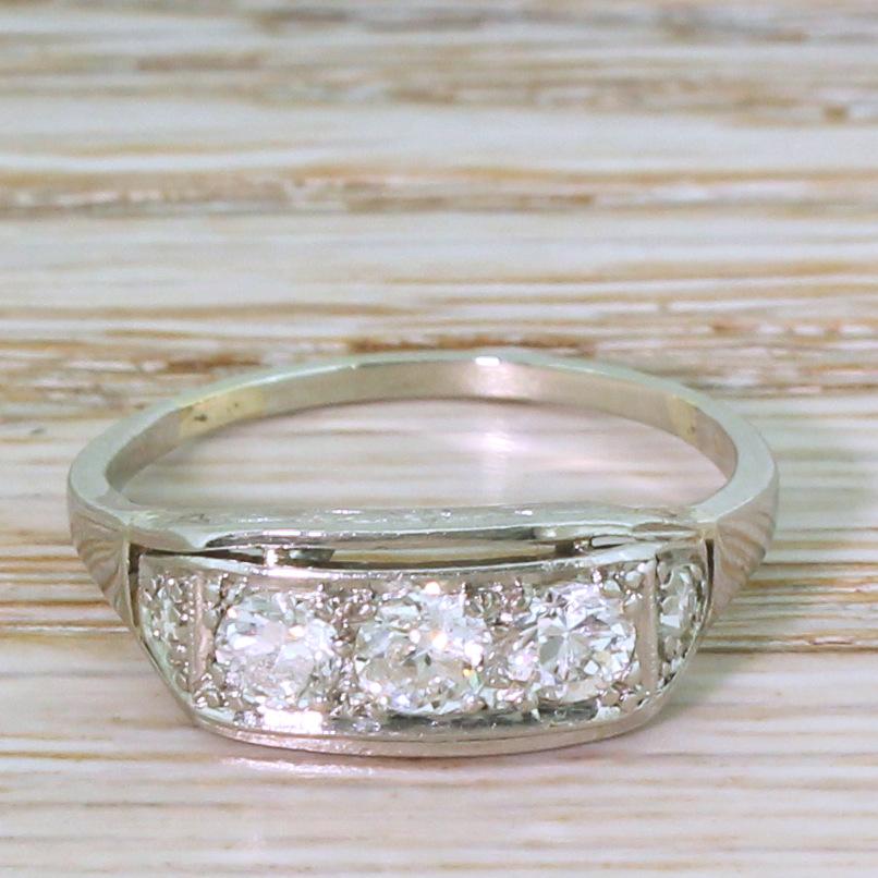 A sleek vintage trilogy ring. The central trio of impressively vibrant old European cut diamonds are bead-set within the rectangular head of the ring, and leads to a trapezoid shaped shoulders each set with a further old European cut. The gallery,