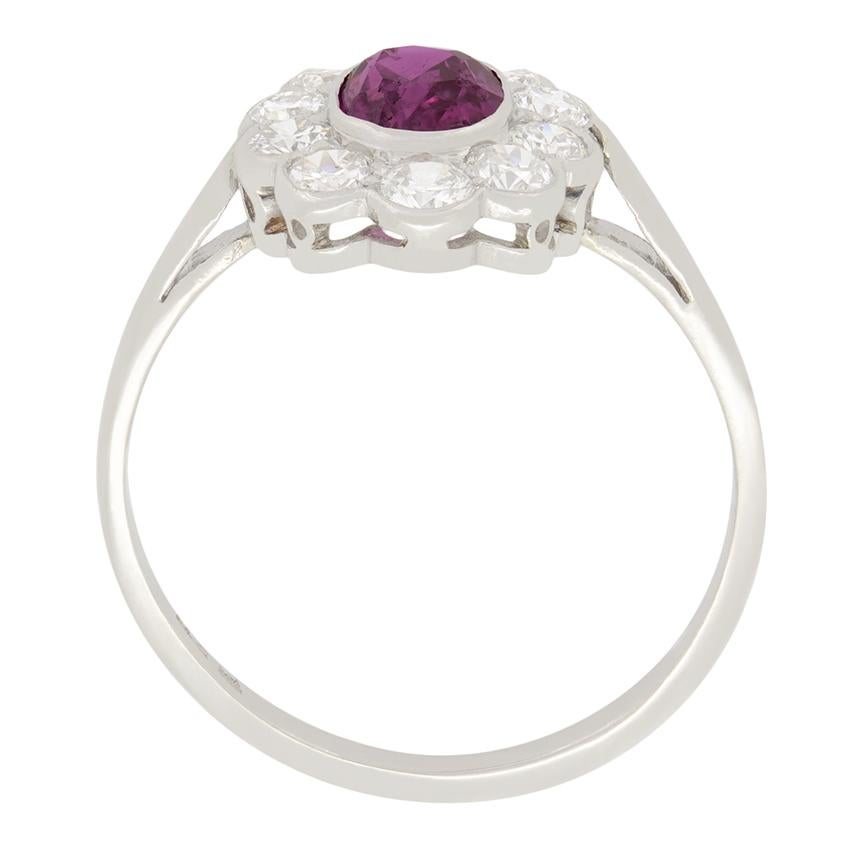 Crafted in the 1920s, this Art Deco era cluster ring features a stunning central pink sapphire surrounded by transitional diamonds. The natural sapphire is an oval cut stone weighing 0.60 carat. The surrounding diamonds are all transitional cut