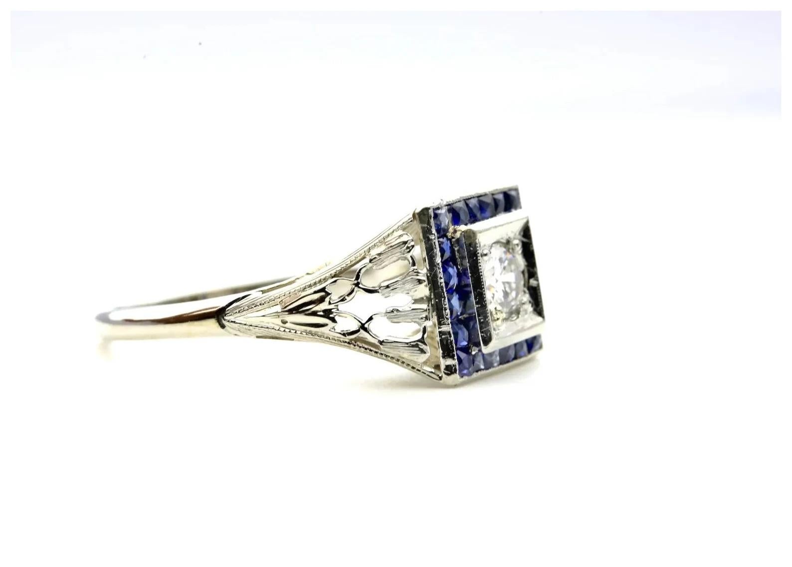 An Art Deco period diamond, and French cut sapphire ring in 18 karat white gold. Featuring a 0.20 carat H color VS2 clarity old European cut diamond surrounded by French cut sapphires. The twenty French cut sapphires weigh a combined 0.40 carats and
