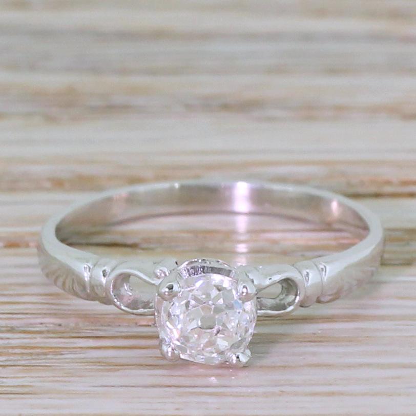 A charming old mine cut diamond engagement ring. The centre stone is glowingly white, internally very clean and alive with brilliance. The diamond is secured in a four claw collet with triangular detailing in the gallery, leading to wonderfully