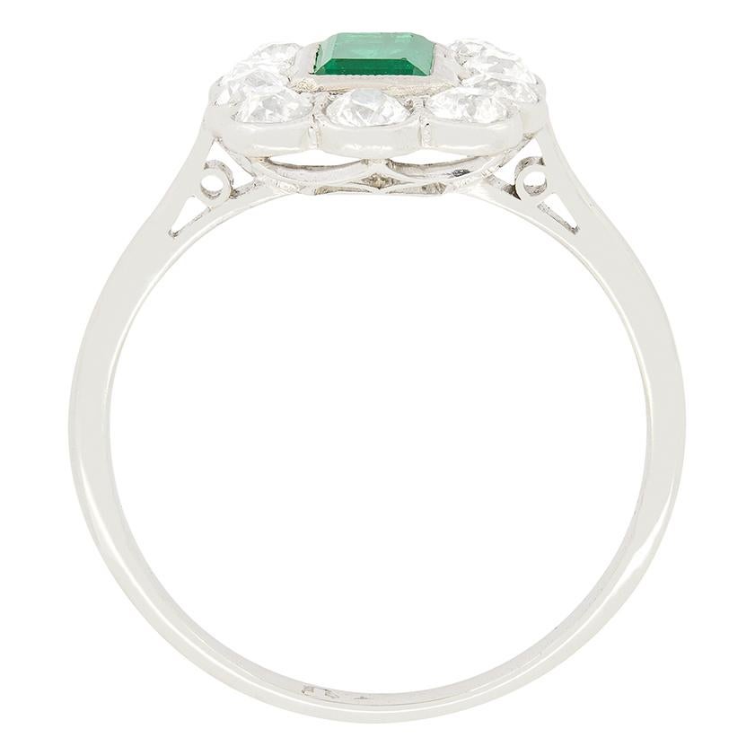 A forest green natural emerald sits pride of place in this Art Deco cluster ring. The lustrous stone is a 0.65 carat, emerald cut and has been rub over set into patterned platinum. Surrounding the central emerald is a halo of ten old cut diamonds