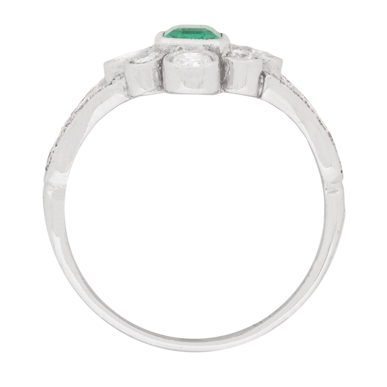 This art deco ring dates back to approximately the 1940s and features a sea green emerald in the centre, weighing 0.70 carat. It is set within an 18 carat white gold rub over setting. In the halo which surrounds the emerald, there are four diamonds