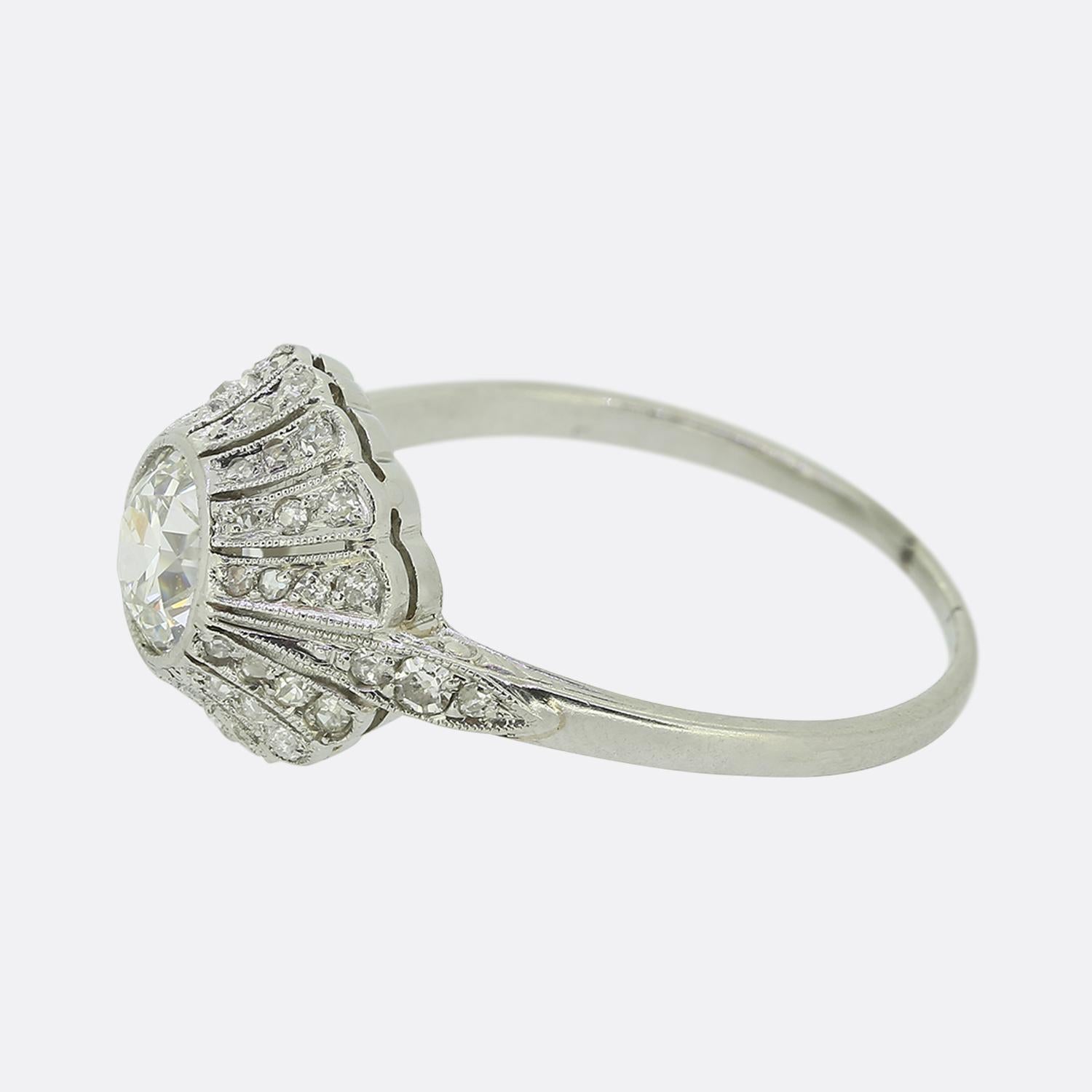 Here we have a charming diamond engagement ring crafted during the pinnacle of the Art Deco movement. This elegant piece showcases an impressive bright white round faceted old European cut diamond at the centre of the face. This principal stone sits