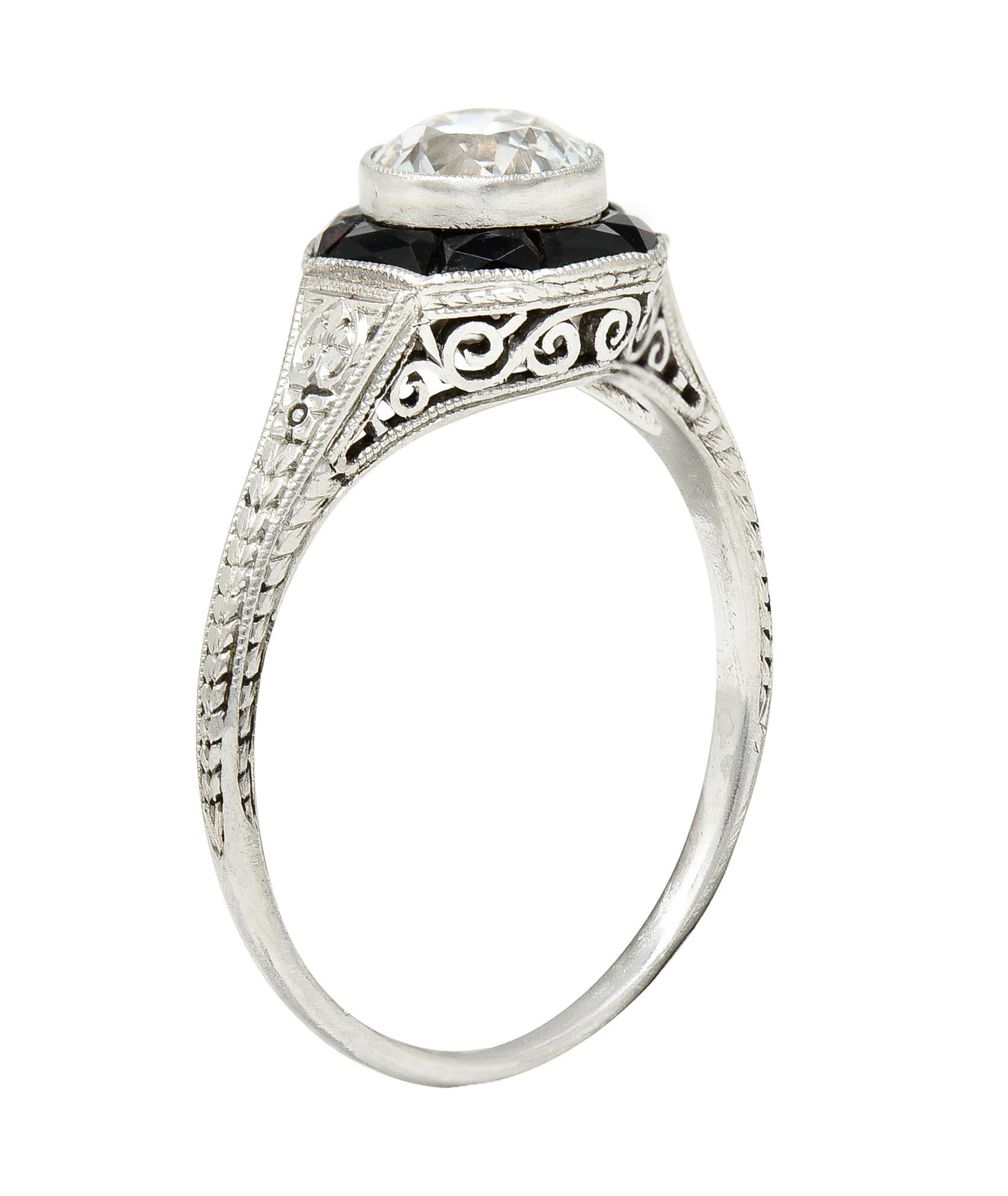 Centering an old European cut diamond weighing 0.70 carat total - H color with VS2 clarity. Bezel set with a recessed halo surround of French cut onyx - channel set in octagonal form head. With a pierced scrolling filigree gallery and flanked by