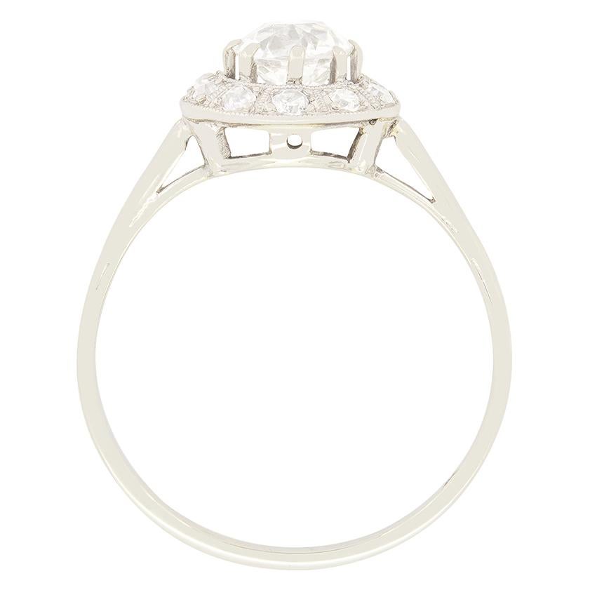 Im Mittelpunkt dieses schönen Art-Déco-Halbrings steht ein 0,74 Karat schwerer Diamant im Kissenschliff. Der funkelnde Stein ist von guter Qualität mit einer Farbe von G und einer Reinheit von VS2. Um den Diamanten herum ist ein Halo aus