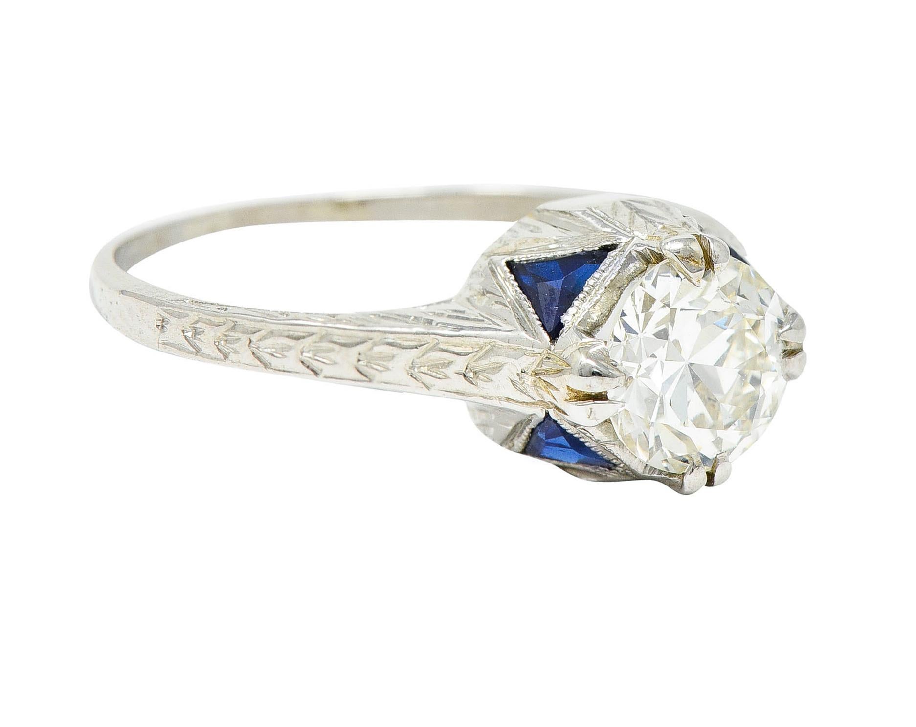 Centering a transitional cut diamond weighing approximately 0.75 carat - K color with SI1 clarity

Set by split prongs and flanked by an engraved wheat motif at shoulders

Accented by calibrè cut synthetic sapphires - medium dark blue

Stamped 18K