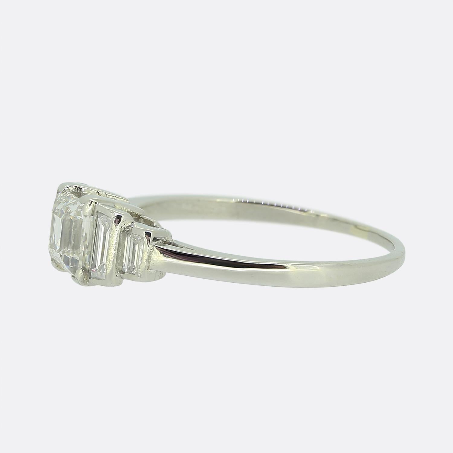 Nous avons ici une élégante bague en diamant fabriquée à l'apogée du mouvement Art déco. Cette pièce en platine présente un seul diamant blanc brillant de taille princesse au centre de la face. Cette pierre principale est ensuite flanquée de part et