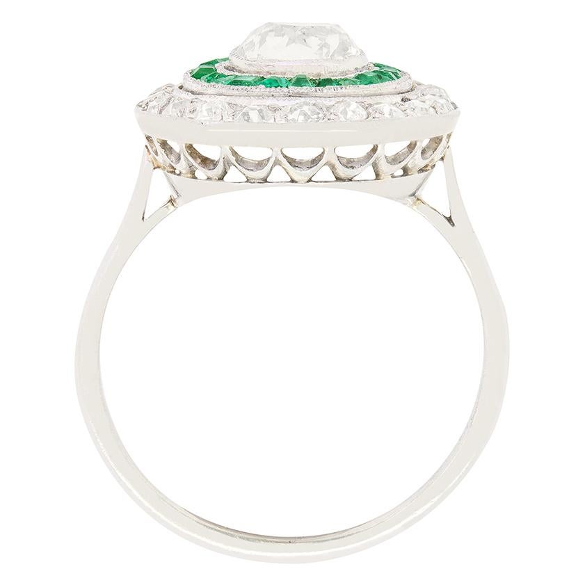 Un superbe diamant de taille ovale ancienne est enveloppé dans des anneaux d'émeraude et de diamant dans cette bague cible Art déco. Le diamant central pèse 0,80 carat et est serti par frottement avec des détails de milgrain. Le cercle d'émeraudes