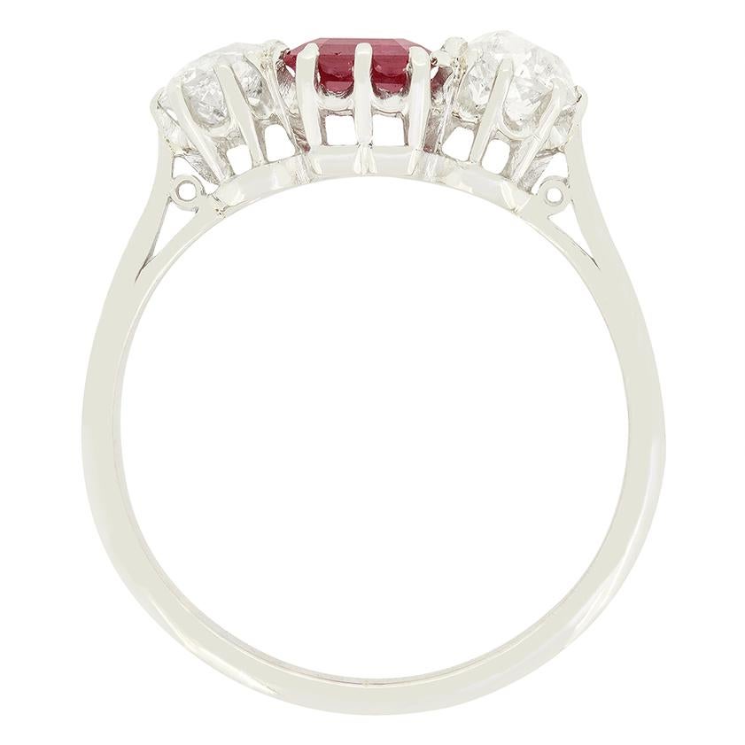 Un vibrante rubino rosso è affiancato da diamanti di taglio antico in questo anello a tre pietre in stile Art Déco. Lo splendido rubino ha un peso di 0,90 carati ed è un taglio smeraldo. La coppia di diamanti, in contrasto tra loro, pesa 0,35 carati
