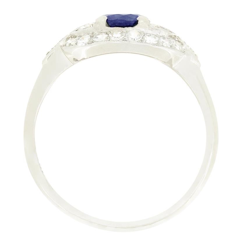 Risalente agli anni '20, questo anello a grappolo unico presenta un intenso zaffiro blu al centro. Lo zaffiro è una pietra di taglio antico del peso di 0,90 carati ed è incastonato a griffe. A complemento dello zaffiro, un meraviglioso gruppo di