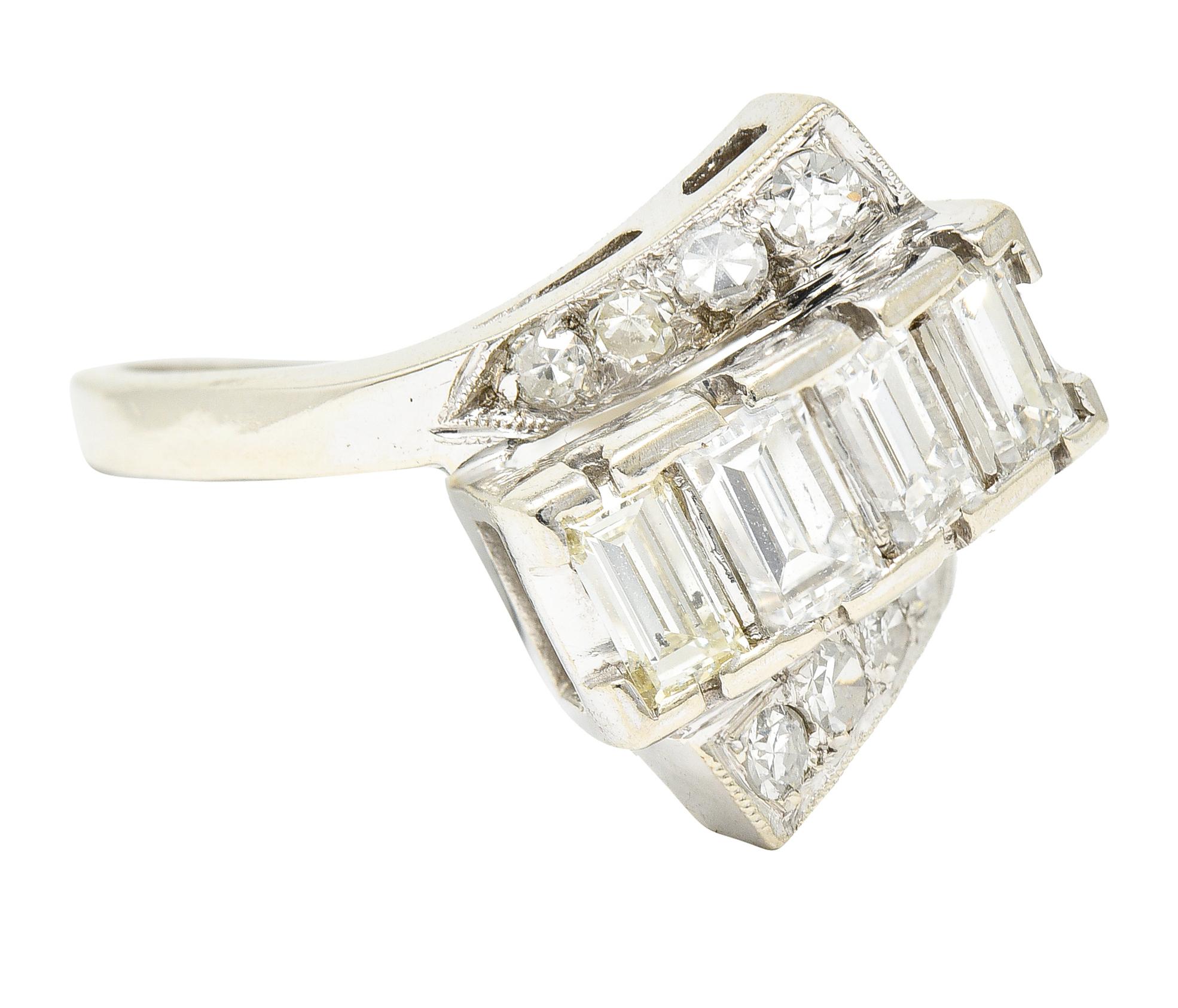 Bypass ring centers a row of straight baguette cu diamonds. Weighing collectively approximately 0.80 carat - G/H color with VS1 clarity. Rectangular form is ori. nted at an angle and flanked by ribbon like shoulders. Accented by single cut diamonds