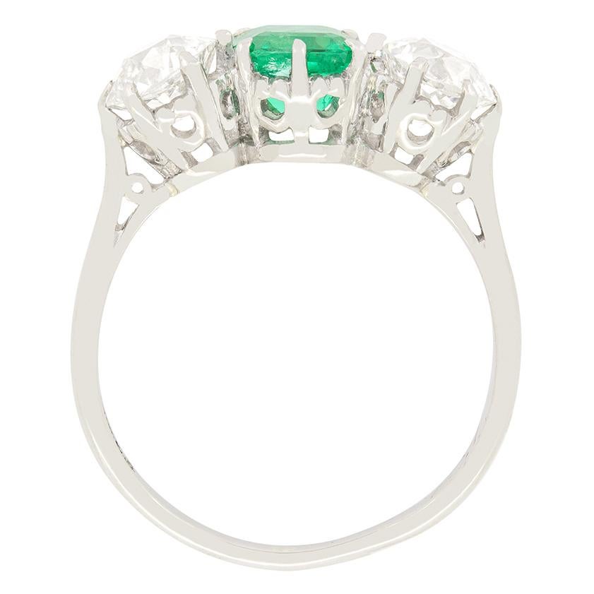 Dieser wunderschöne Ring aus den 1920er Jahren zeigt in der Mitte einen leuchtend grünen Smaragd, flankiert von einem Paar Diamanten im Altschliff. Er wiegt 1,00 Karat und ist in der traditionellen Smaragdform geschliffen. Im Kontrast zum zentralen