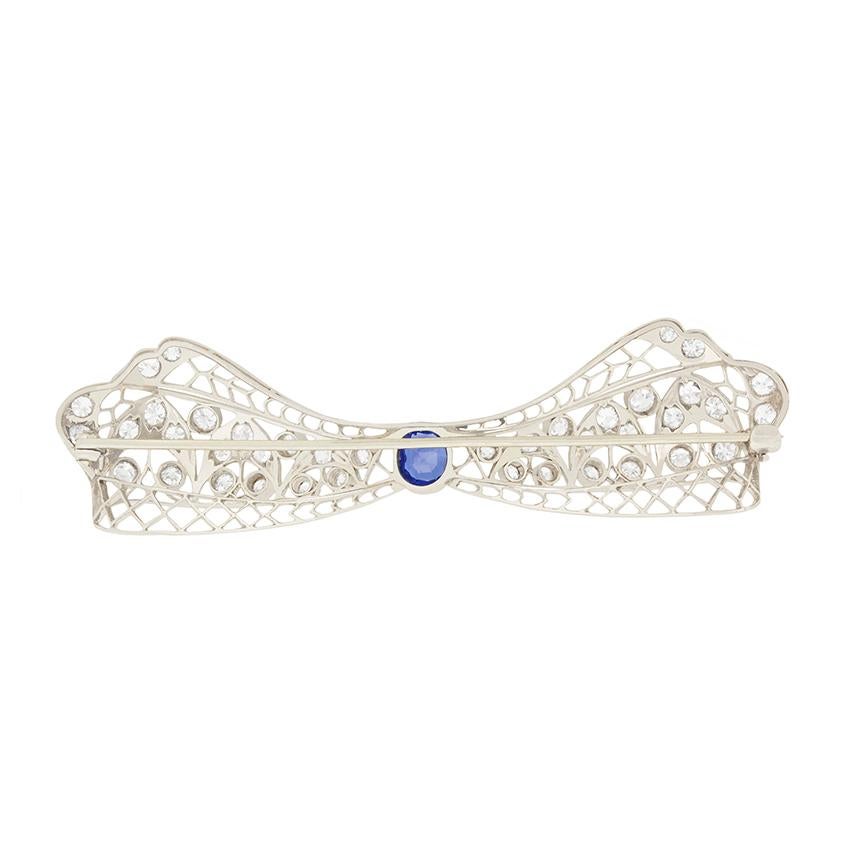 This wonderfully delicate art deco brooch takes the form of a bow, and is embellished with diamonds and a sapphire. The old cushion cut sapphire is 1.00 carat, and is a deep blue colour. The framework of the bow is set with old cut diamonds,