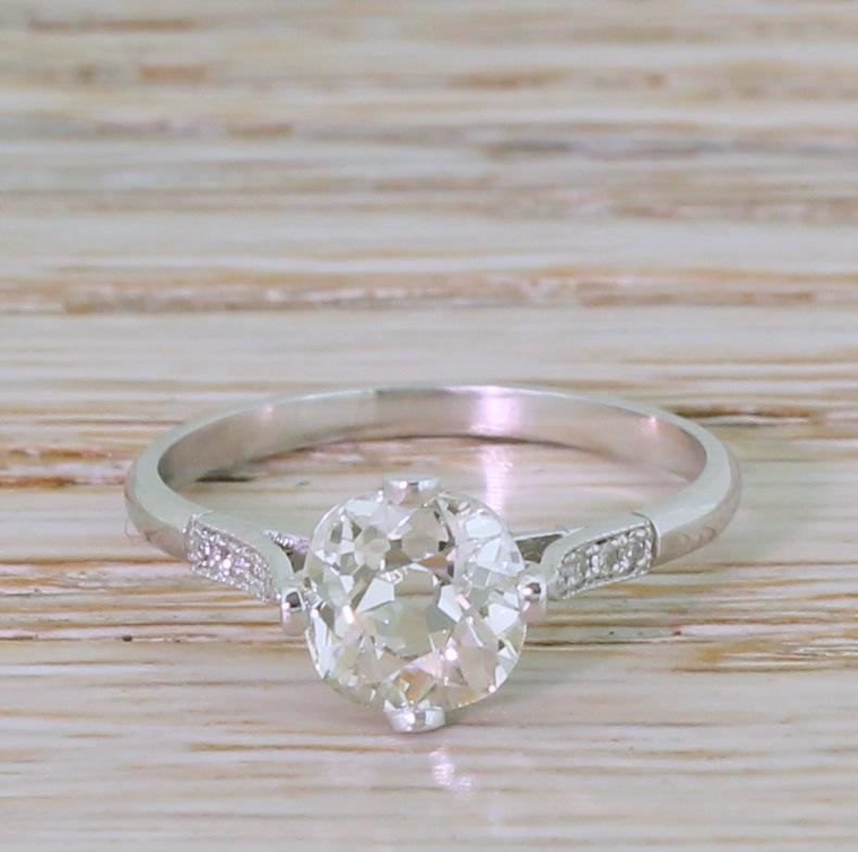 A belter of an Art Deco engagement ring. The centre stone – graded by HRD Antwerp as I colour, VVS2 clarity – is glowingly white and internally very clean. Four claws at compass point secure the cushion shaped diamond in a very pretty low collet