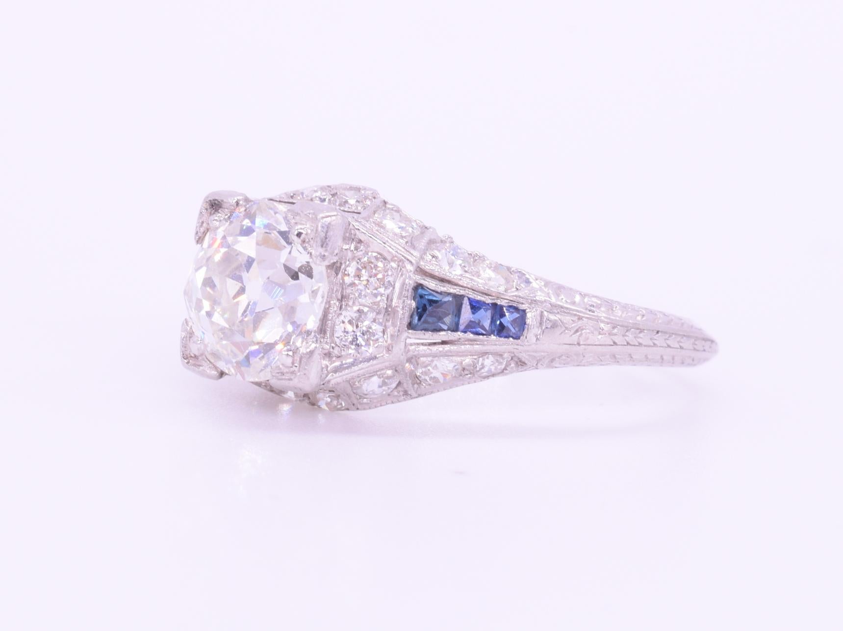 An old European cut diamond weighing approximately 1.04cts, of approximately I color and SI clarity is accented with calibré sapphires totaling approximately  0.15ct and round diamonds totaling approximately 0.40ct mounted in platinum with
