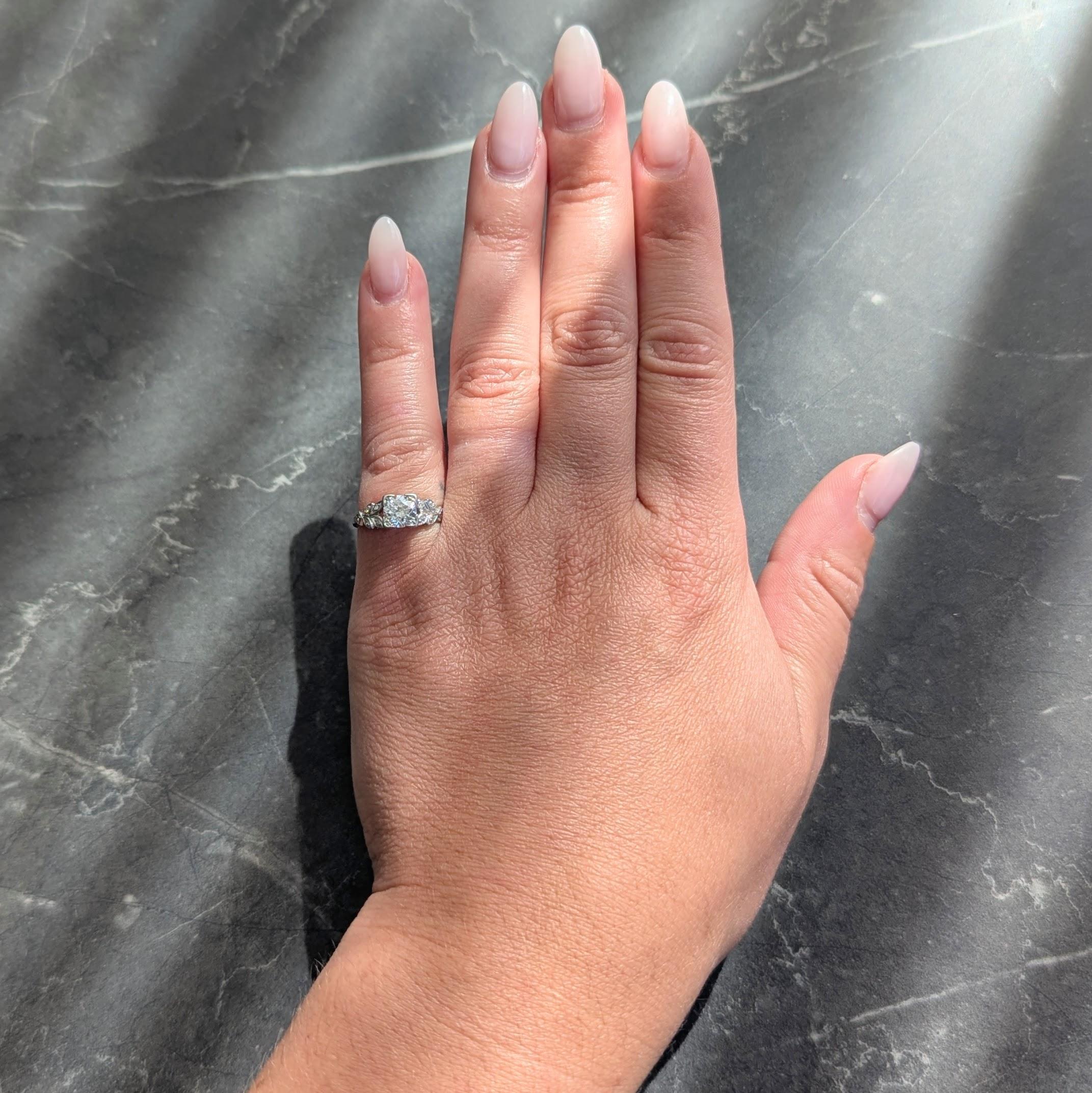 Al centro un diamante vecchio taglio europeo di circa 0,93 carati - colore H e purezza VS2.
Incastonato con tre punte di perline in una testa a forma di quadrato e affiancato da spalle a cattedrale.
Disegnato come un motivo fogliare a più livelli e