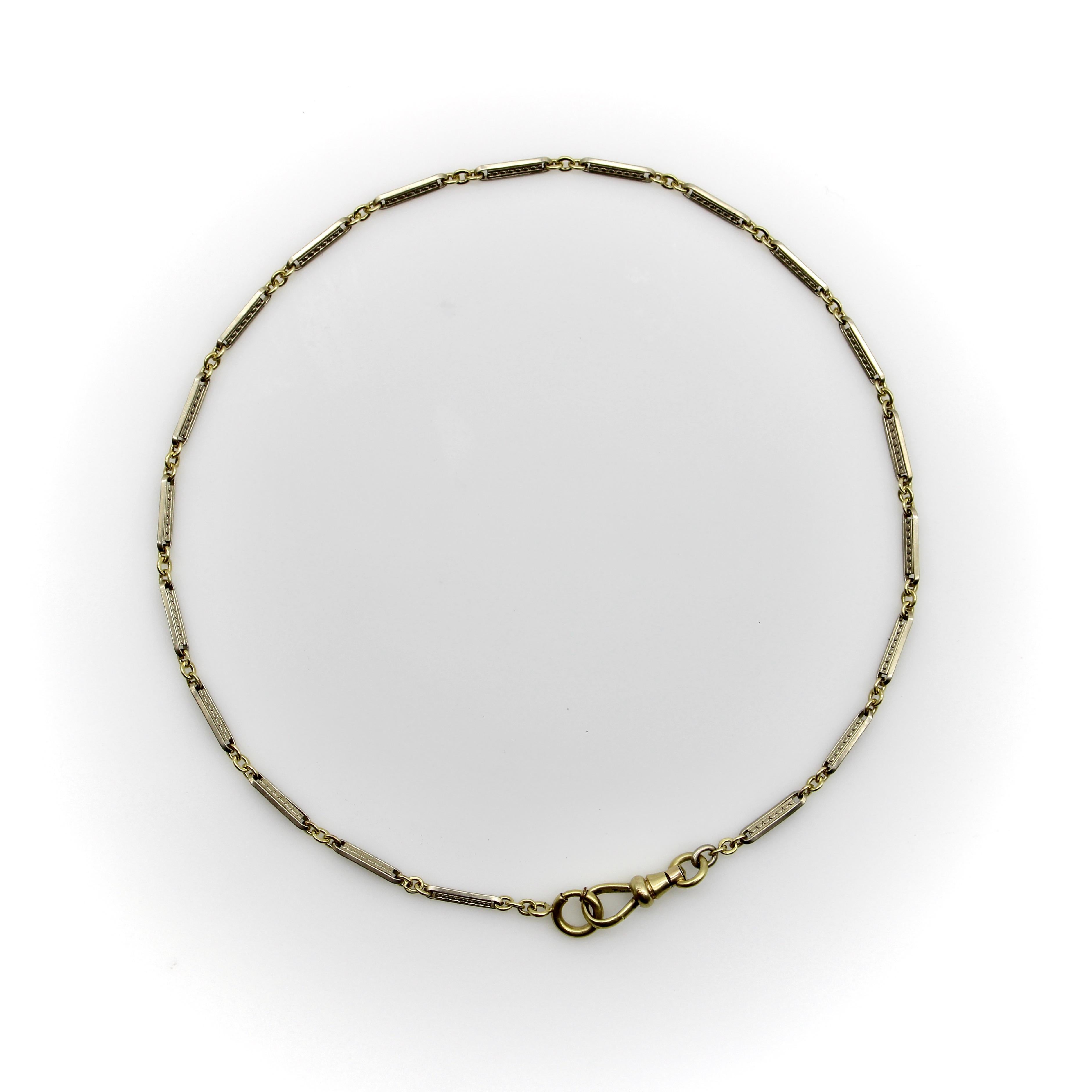 This is a versatile Art Deco watch chain, made up of a series of 10k white gold bar links with embossed decoration on them. Between the bars are yellow gold links that hold the chain together, for a nice cool/warm chain of alternating white and