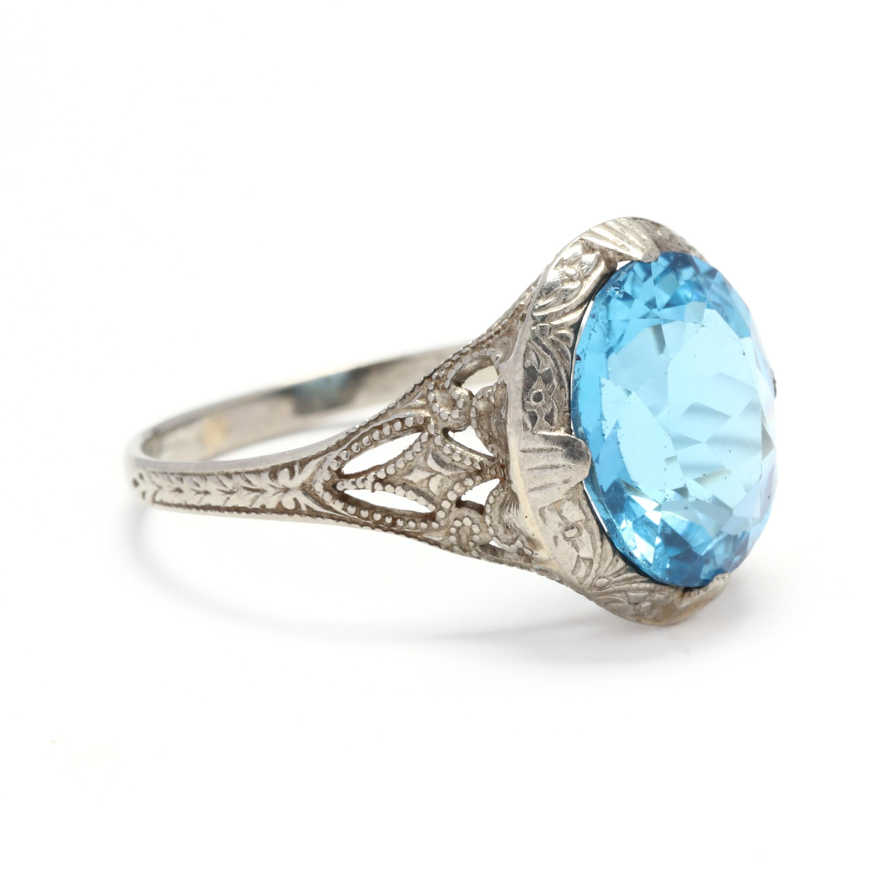 An Art Deco 10 karat white gold and blue topaz filigree ring. This ring is centered on a prong set, oval cut blue topaz stone weighing approximately 3.6 carats set in an engraved filigree mounting with milgrain detailing.

Stones:
- blue topaz, 1