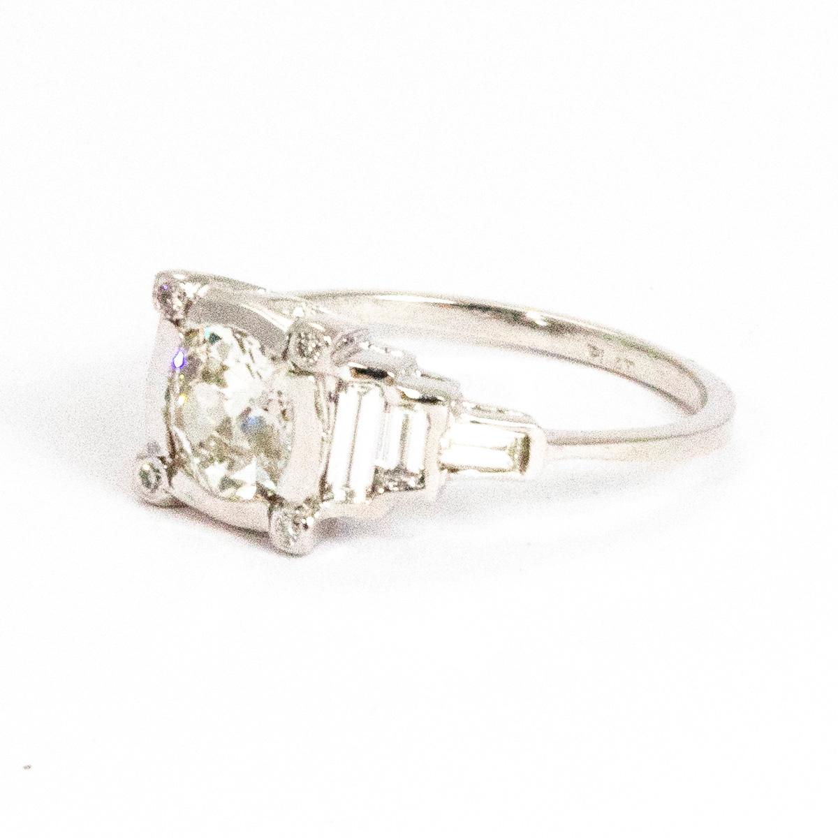 The gorgeous centre diamond measures 1.10ct and is old mine cut. Around the diamond in each corner of the square shaped setting sits a diamond point. This ring has an Art Deco style reflected in the horizontal baguette diamonds which create step